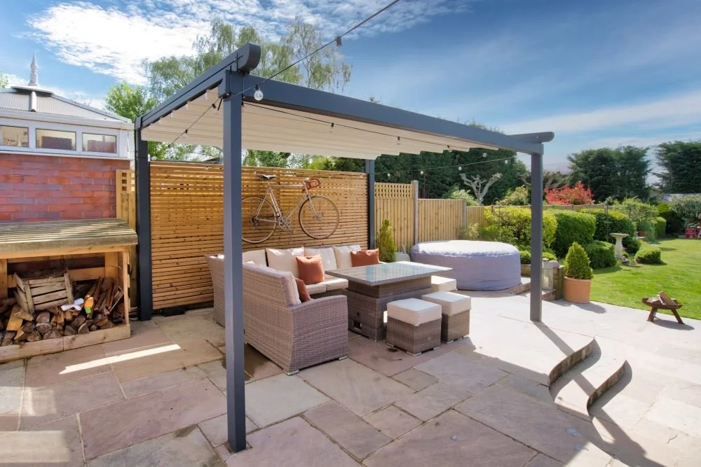 Backyard patio with outdoor furniture, a bike mounted on a wooden privacy fence, and a garden with bushes and trees under a partly cloudy sky.