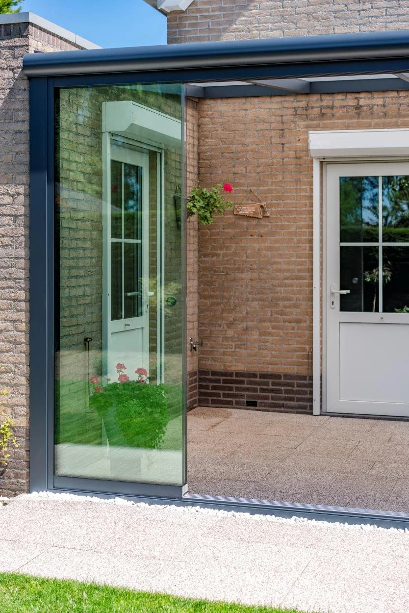 A sliding glass door leading to a patio with brick walls and a white door with window panes, green plants, and a red flower in a pot visible inside.