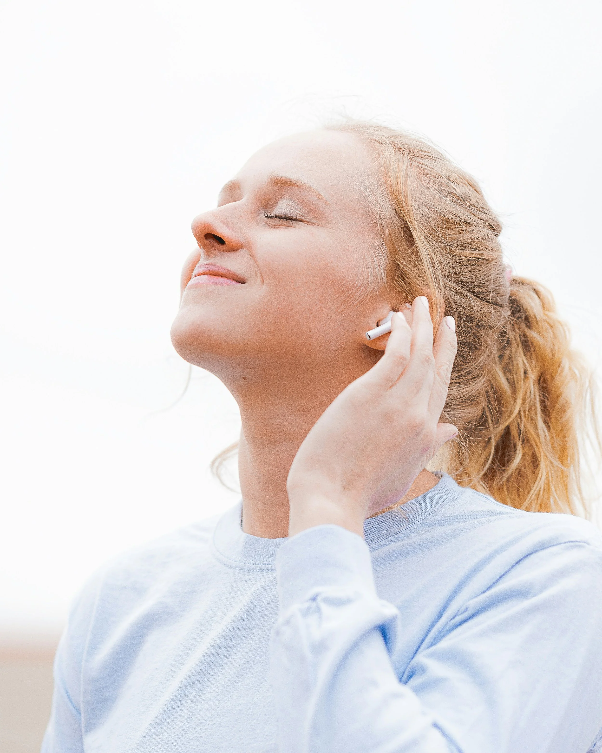 Person with eyes closed wearing earbuds, pausing to listen inward and check in with their body
