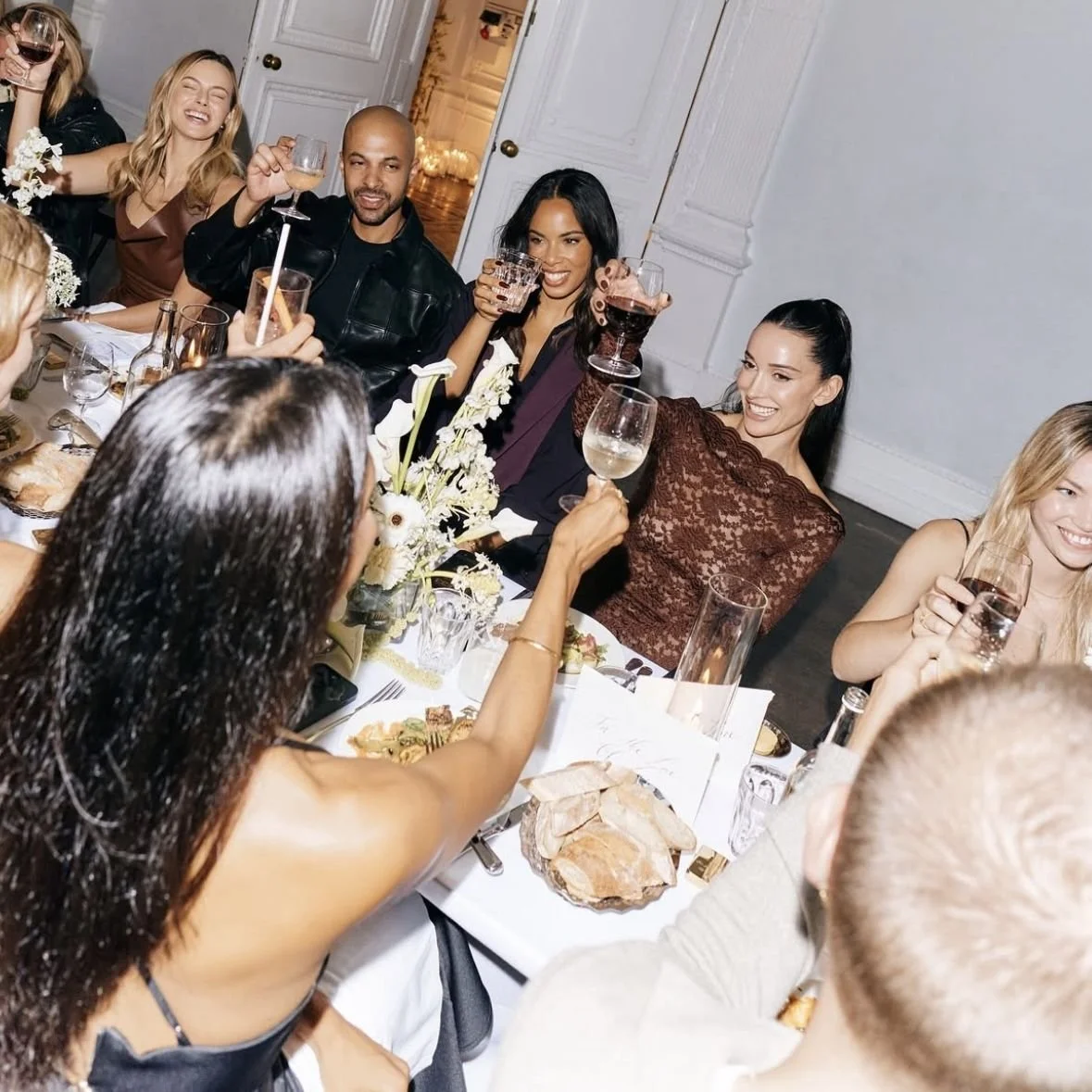 Group of friends celebrating at a dinner party, raising wine glasses and smiling.