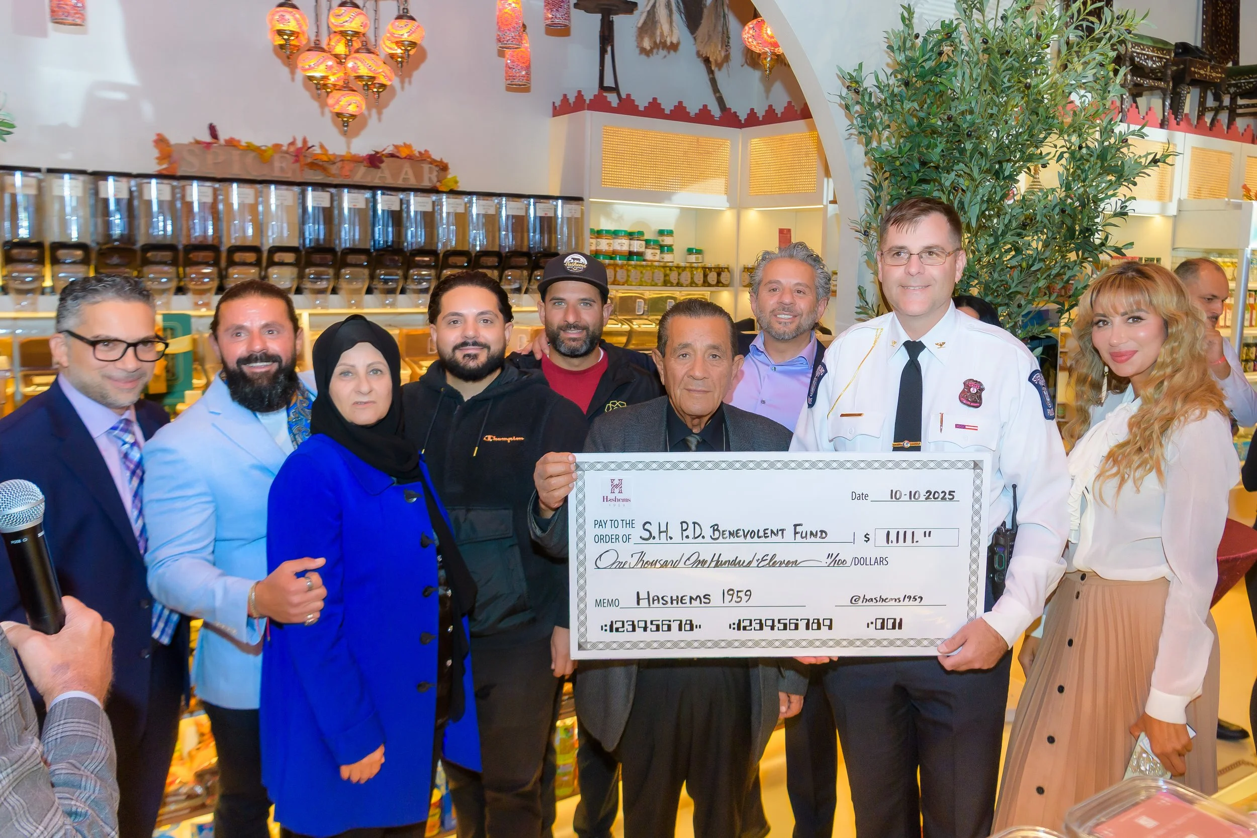 Group of people standing together, holding a large check for a non-profit event. The check is made out to the "S.H.P.D. Benevolent Fund" for $1,111, dated October 10, 2025.