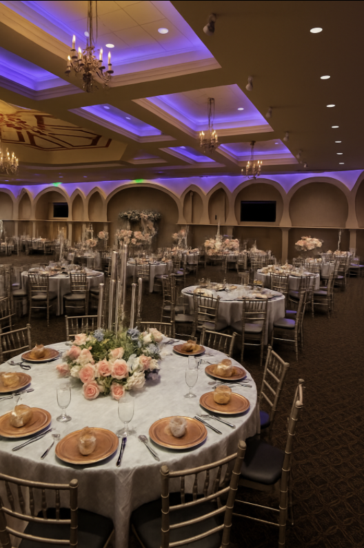 Elegant banquet hall decorated for a wedding or event with round tables, floral centerpiece, gold chairs, and purple ceiling lighting.