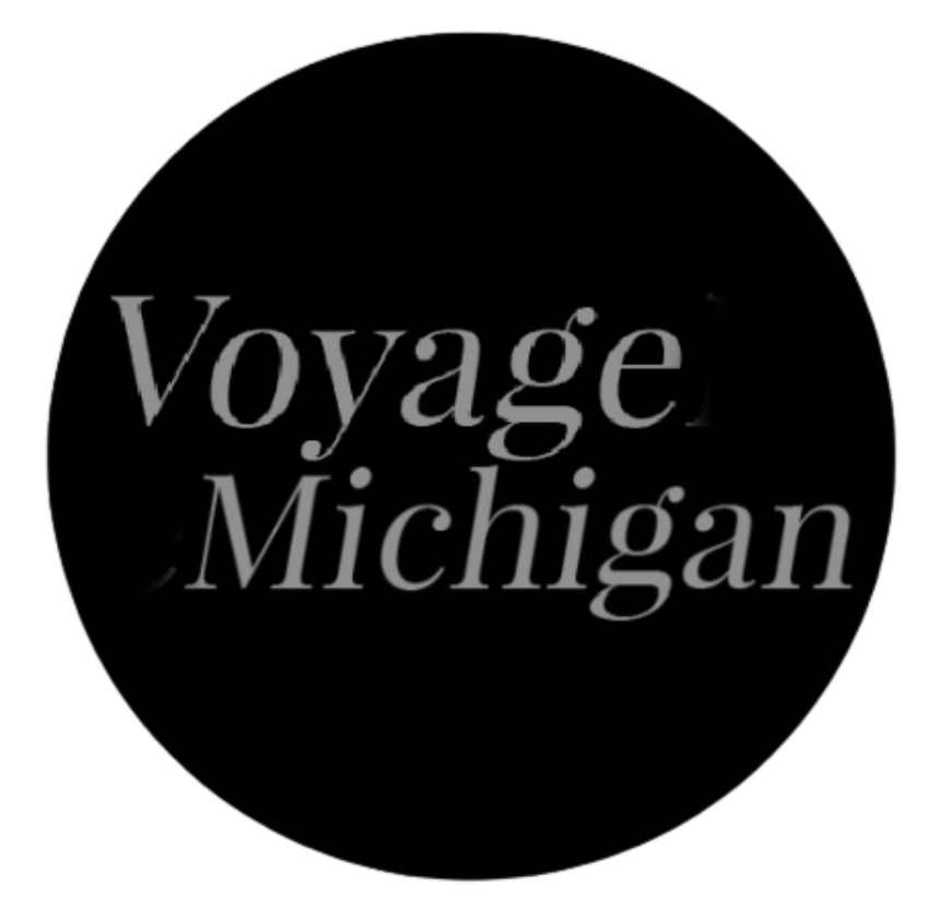 A black circle with the text "Voyage Michigan" in gray, stylized font.
