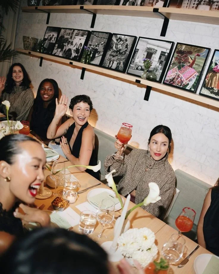 A group of women enjoying a celebratory meal at a restaurant, with some raising glasses and smiling.