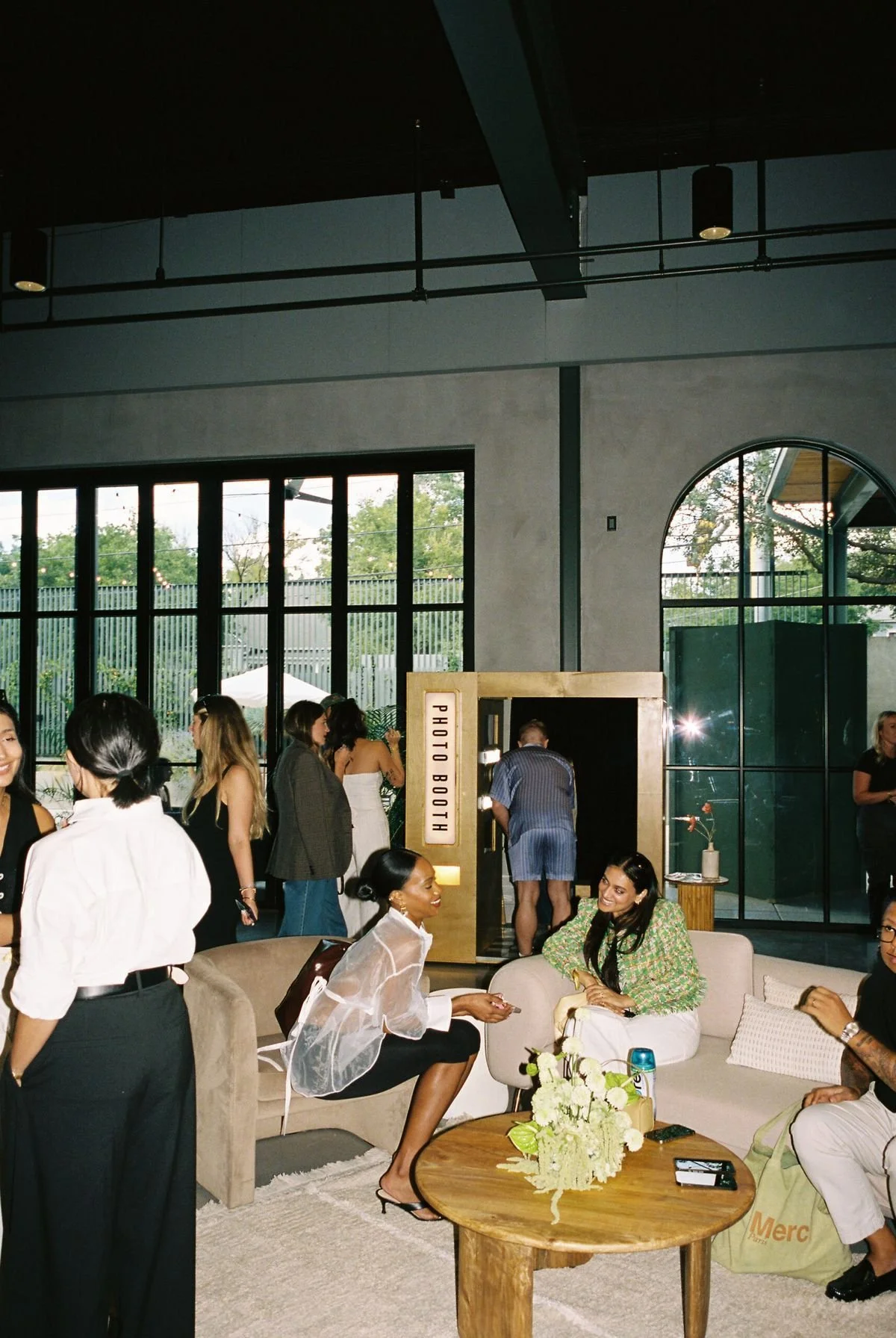 People socializing in a modern indoor space with a photo booth, large windows, and contemporary furniture.