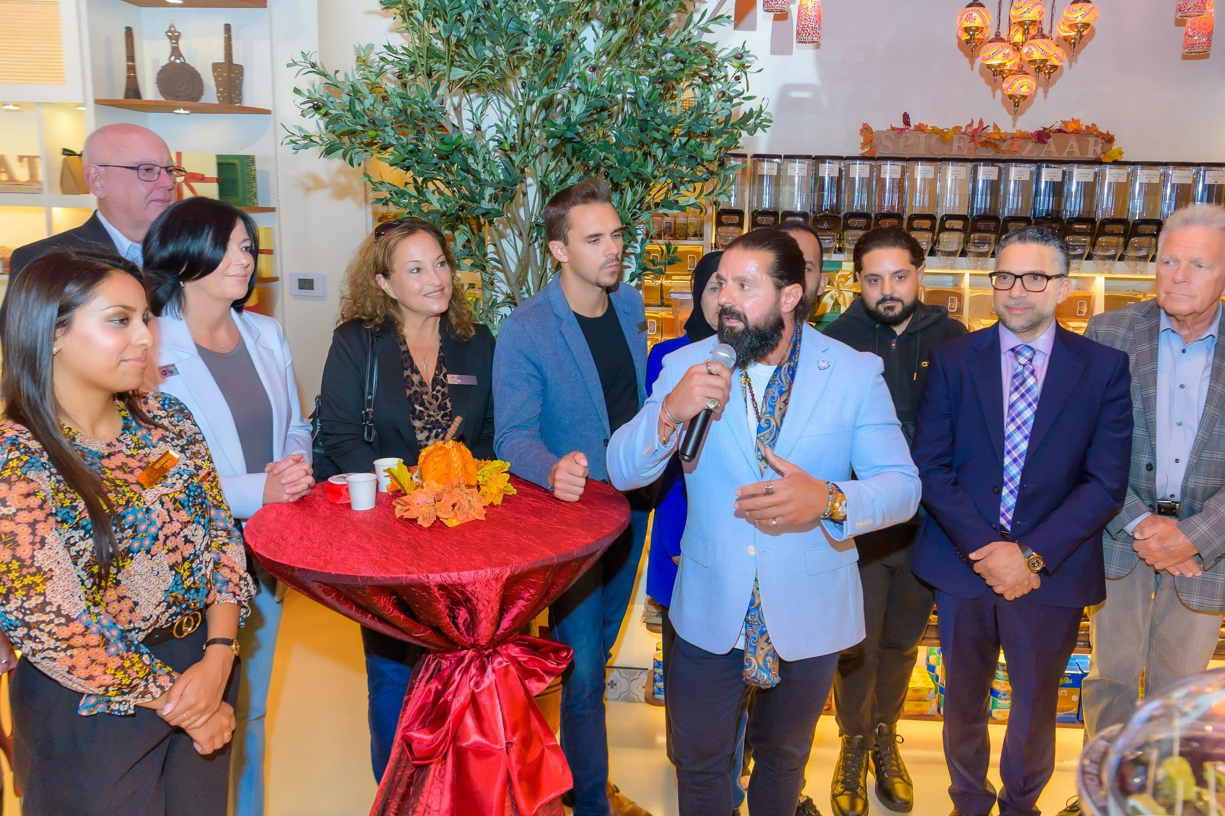 A man in a light blue blazer speaking into a microphone at a non-profit event, with a decorative table