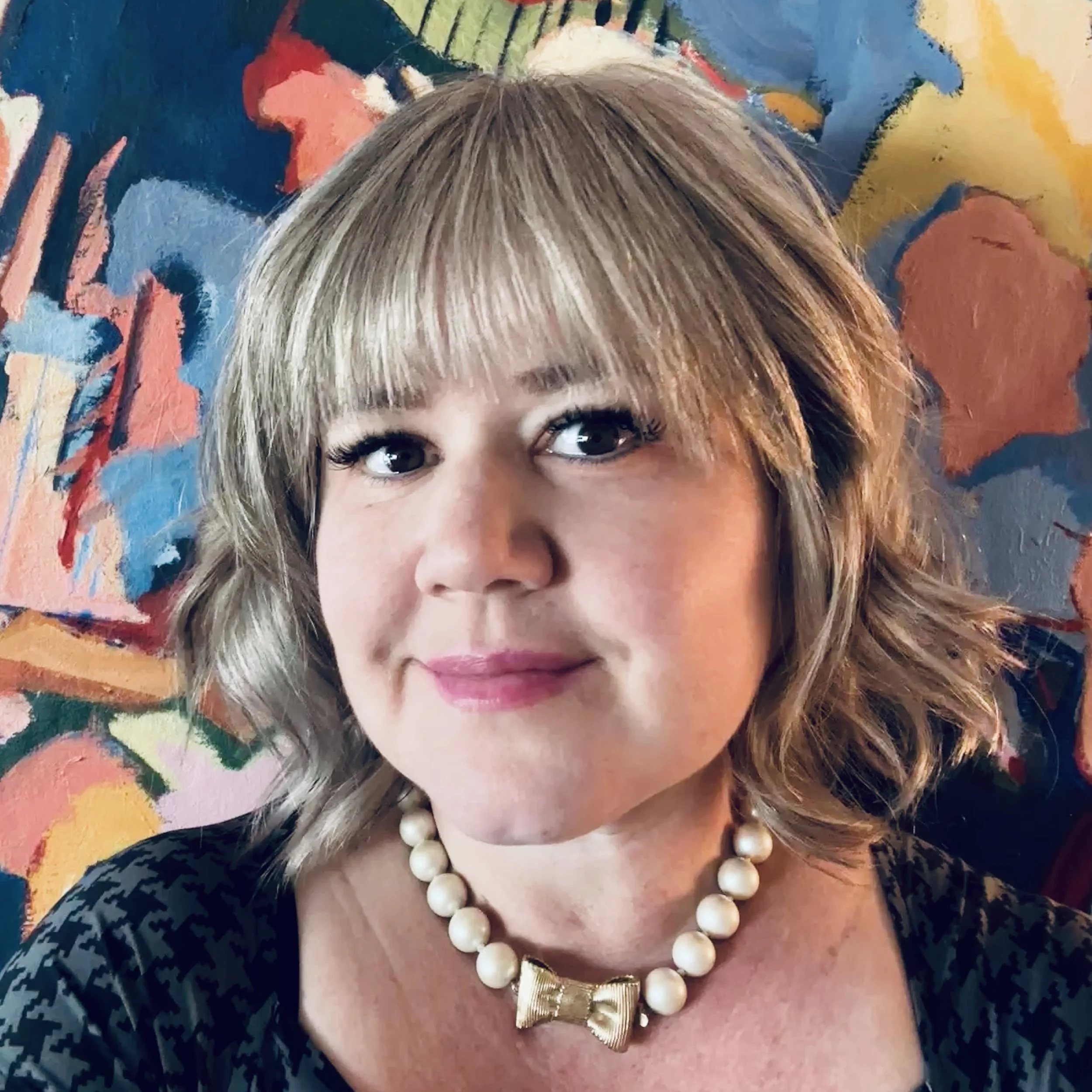 Photograph of a woman standing in front of a colorful abstract painting in an indoor setting.