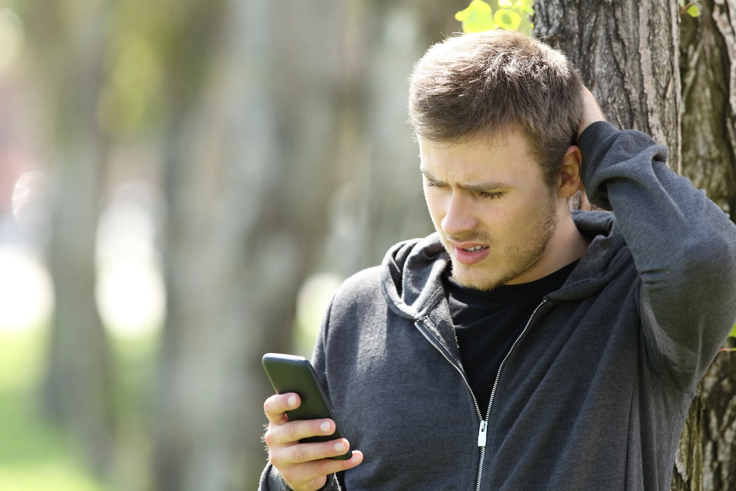 Young man holding a phone, looking down at a NFSI AlertNet gun breach advisory along with an image of the person of interest, allowing for precautionary measures.