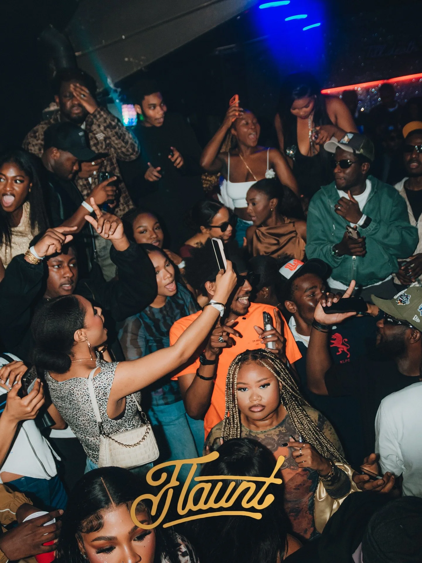 A diverse group of people at a party or concert, some taking photos or videos, some singing or dancing, with a colorful illuminated background and the word 'Haunt' written in gold text at the bottom.