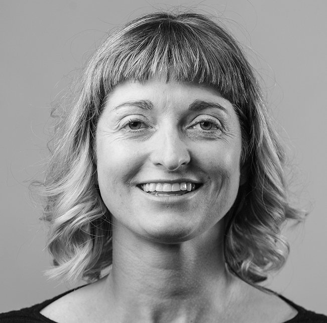 Black and white portrait of a woman with shoulder-length wavy hair and bangs, smiling at the camera.