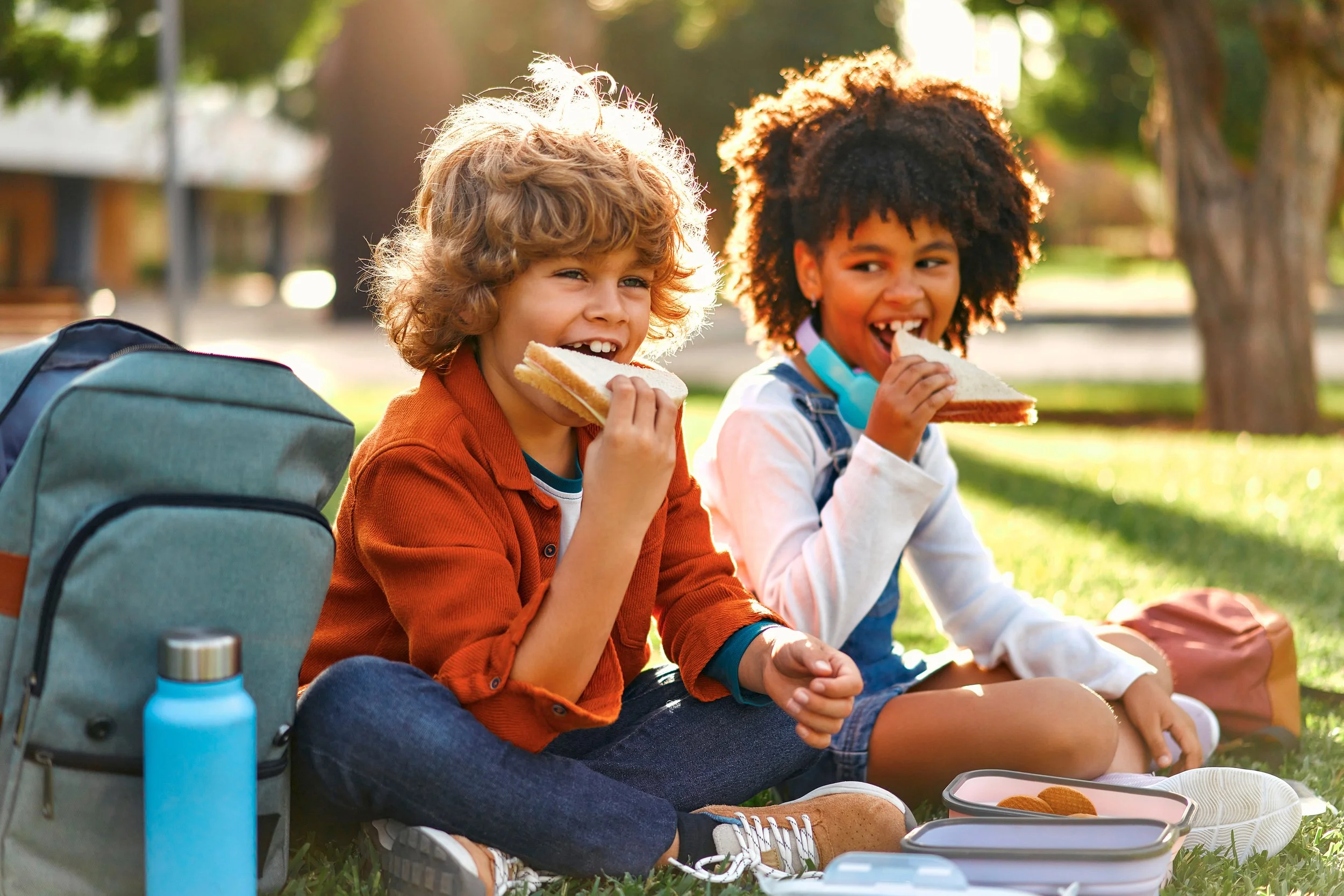 Groep lachende jonge kinderen op school, met rugzakken, binnen in schoolgebouw.