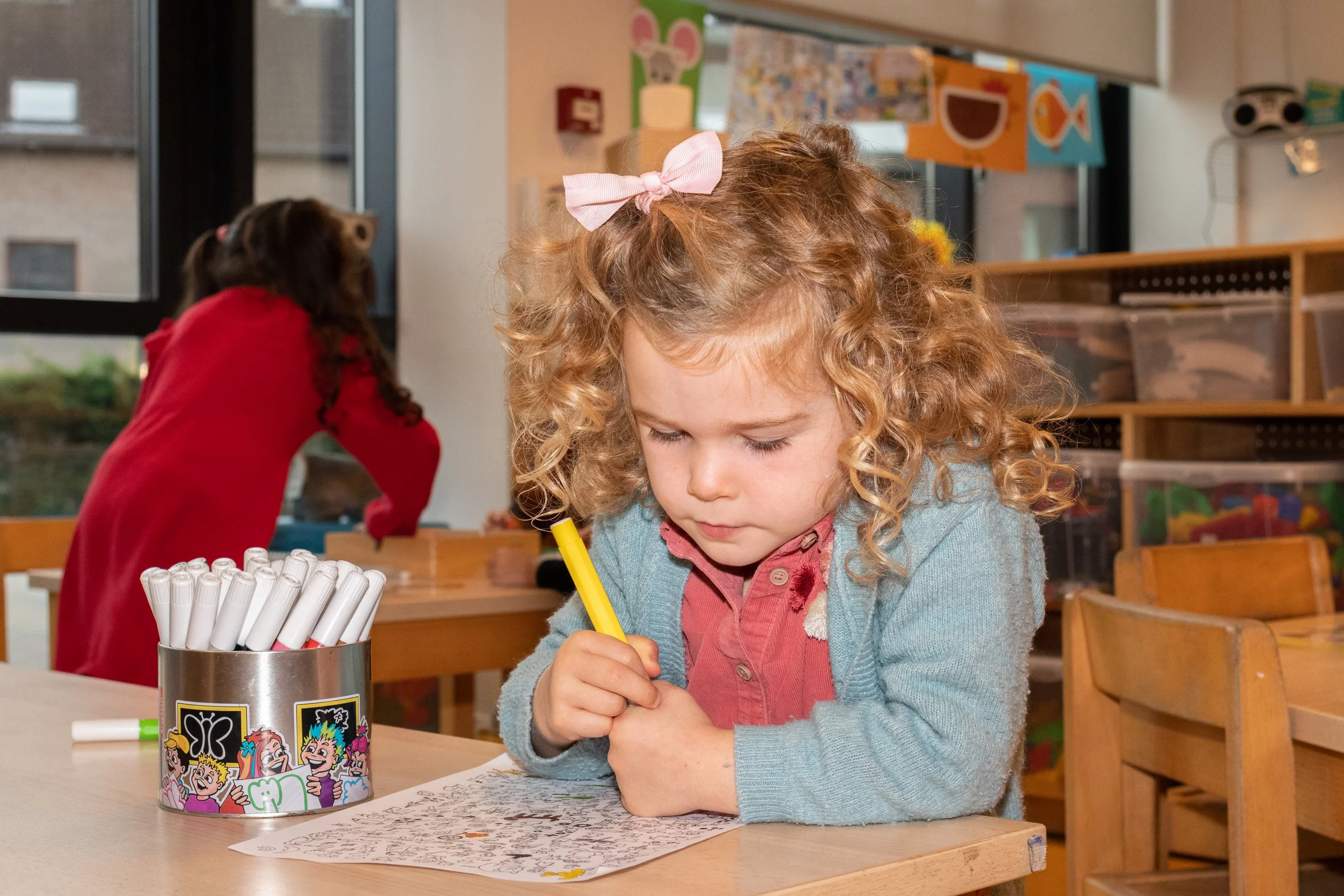 Groep lachende jonge kinderen op school, met rugzakken, binnen in schoolgebouw.