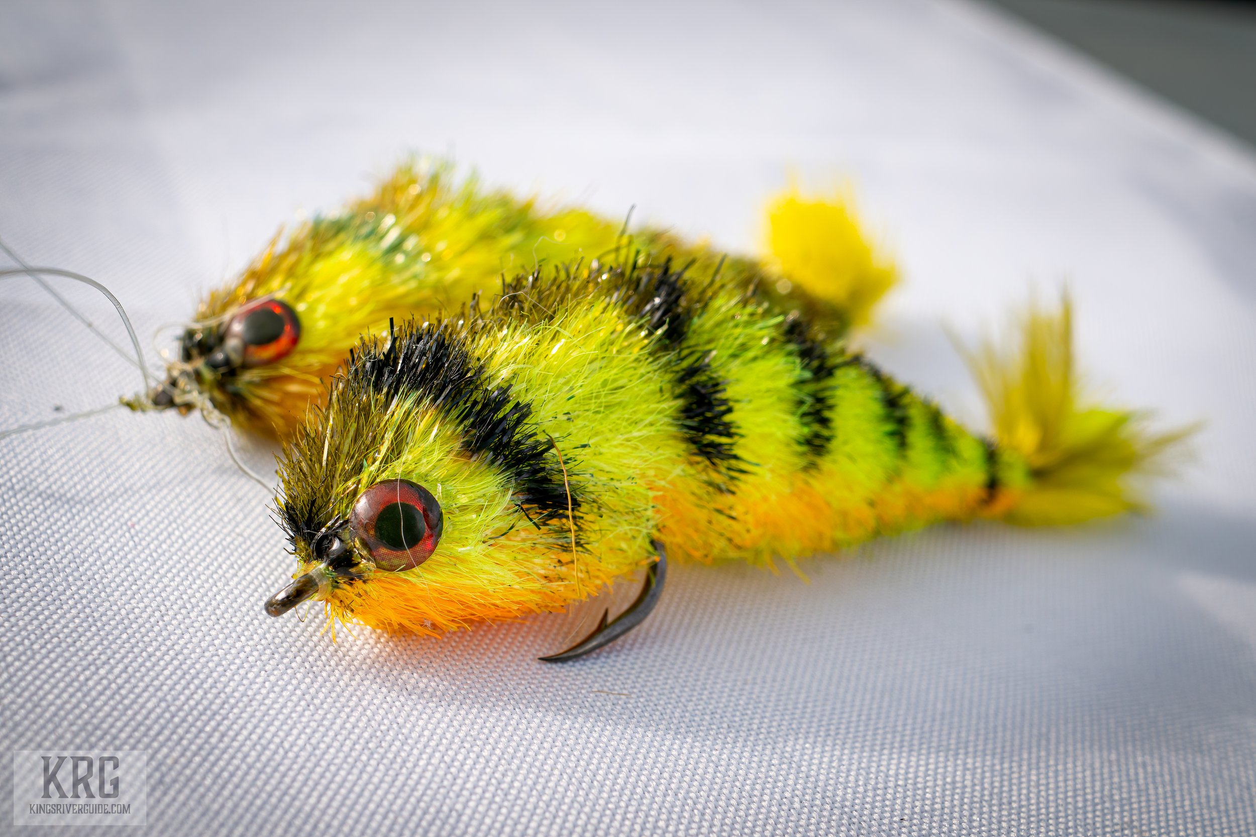 Colorful fishing lures resembling caterpillars with black, yellow, and orange markings, resting on a white textured surface.
