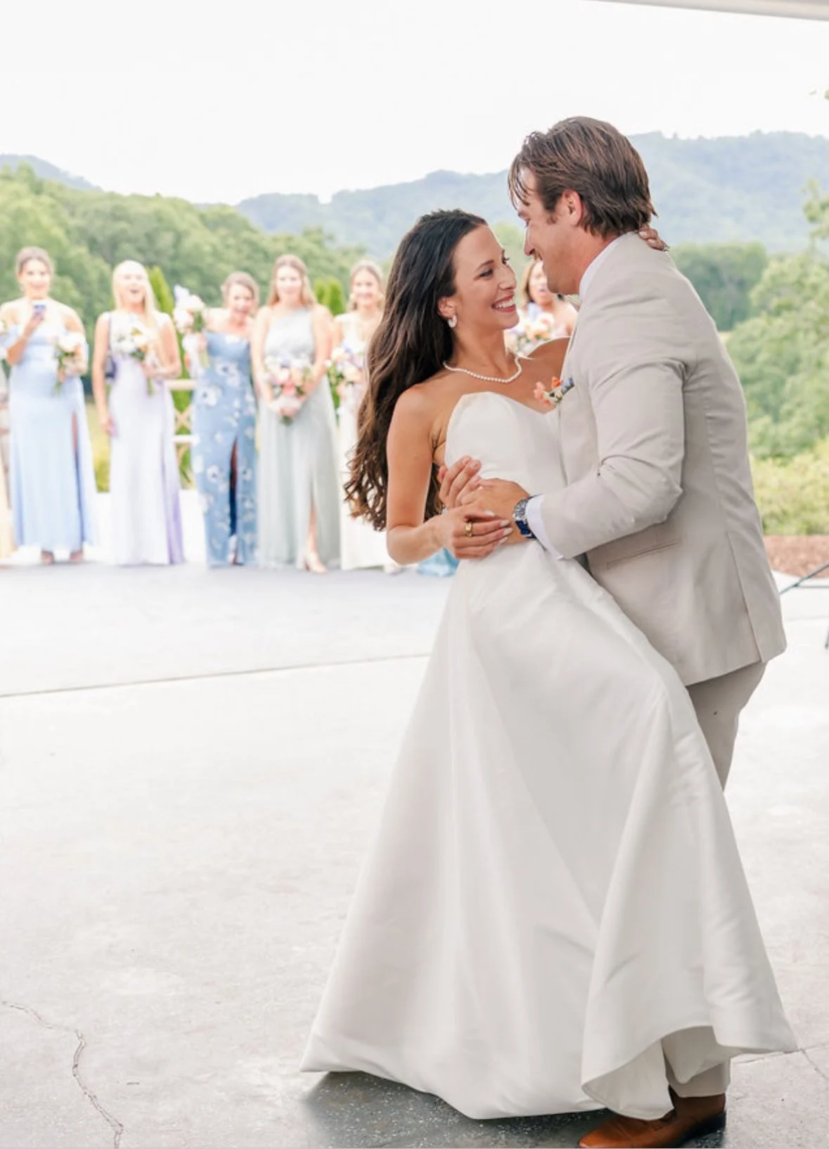 Couple dancing at wedding with bridesmaids in background.