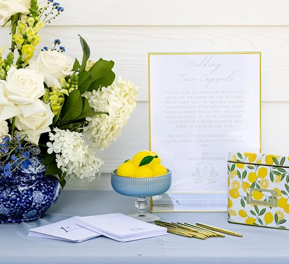 Table setup with white and yellow flowers, a bowl of lemons, wedding invitation, and stationery.