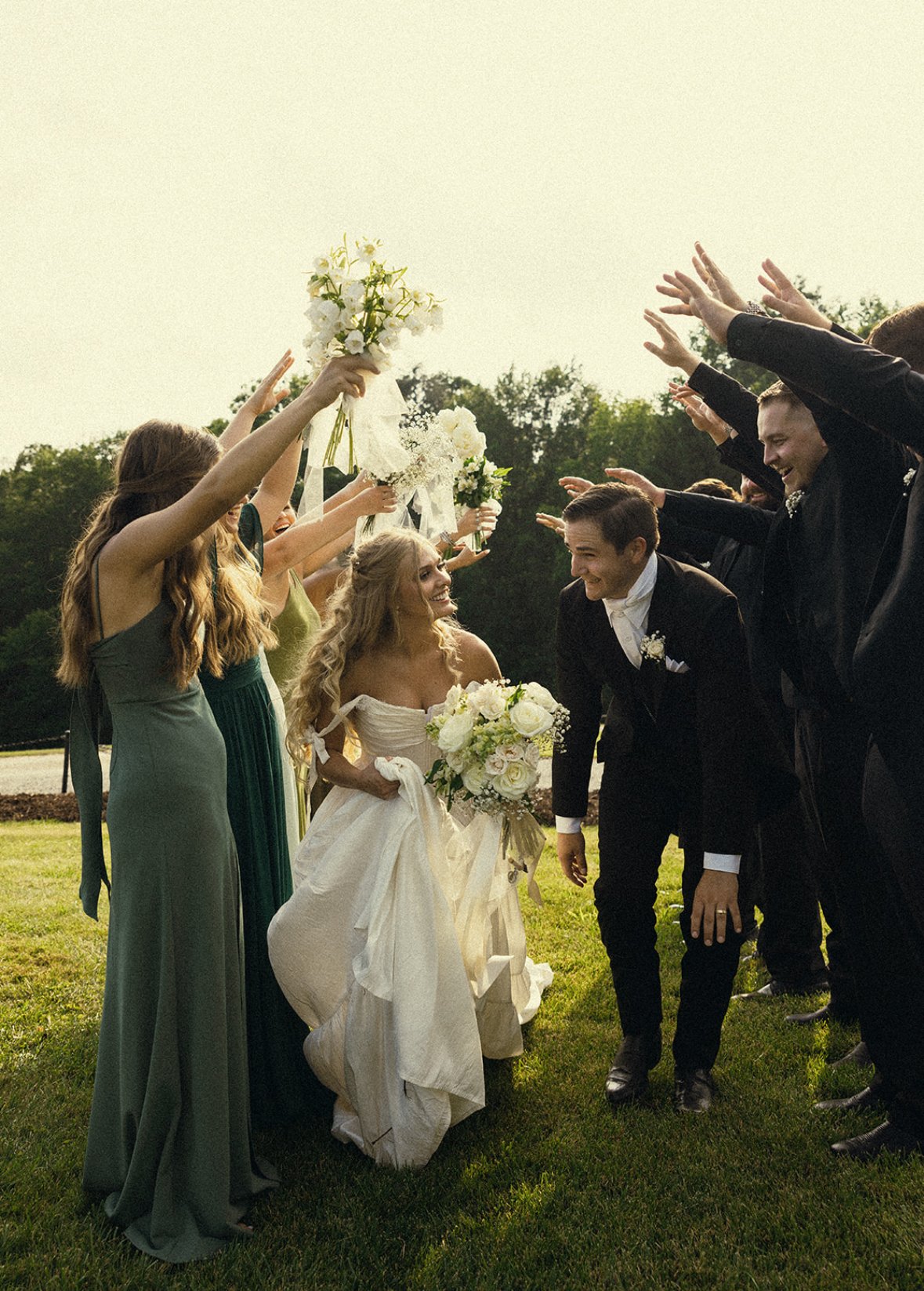 Bride and groom celebrating their wedding outdoors, surrounded by friends tossing flower bouquets in the air.