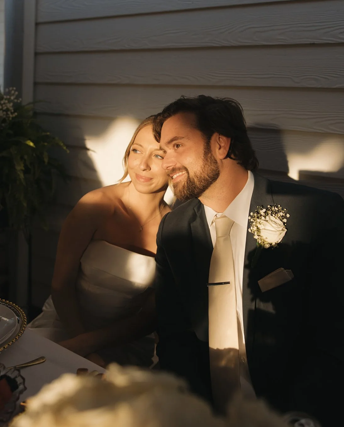A couple, dressed in wedding attire, sitting closely together with warm lighting creating a romantic mood.
