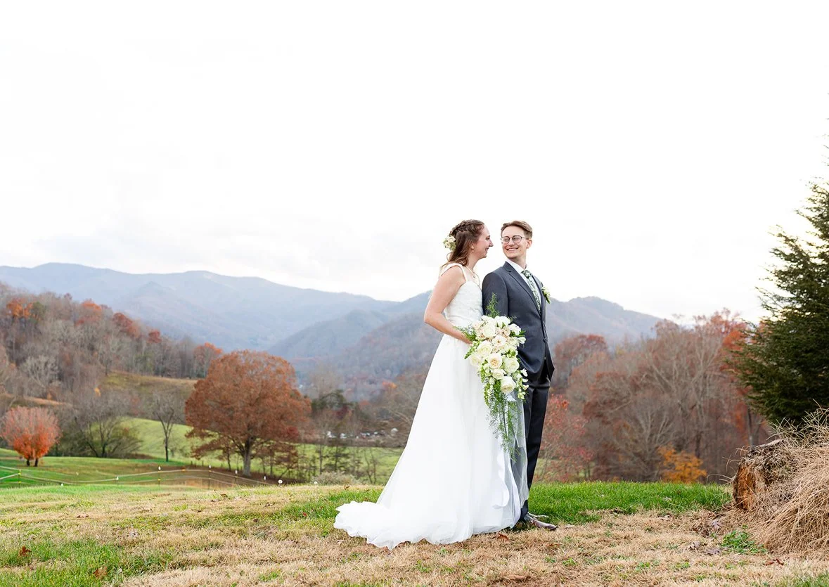 A bride and groom enjoying their wedding outdoors with mountain scenery and autumn trees in the background.