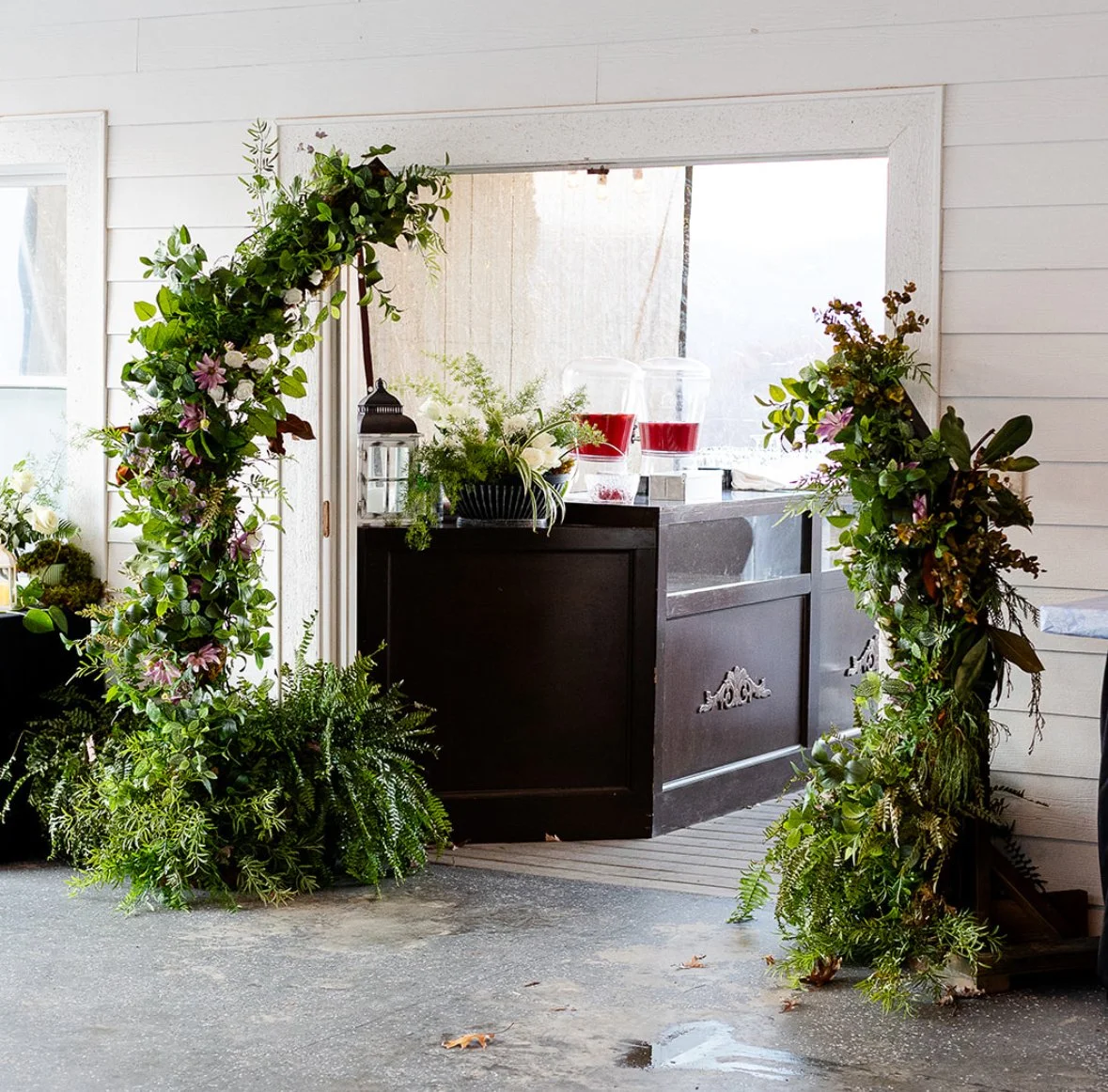 Decorative floral archway framing a coffee bar in a white wooden room with a concrete floor.