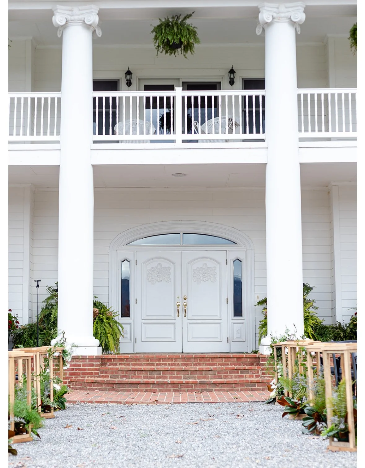 White house entrance with double doors, brick steps, two large white columns, and some greenery on either side.