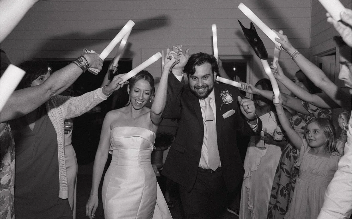 People celebrating at a wedding reception, walking through a tunnel of lit glow sticks held by guests.
