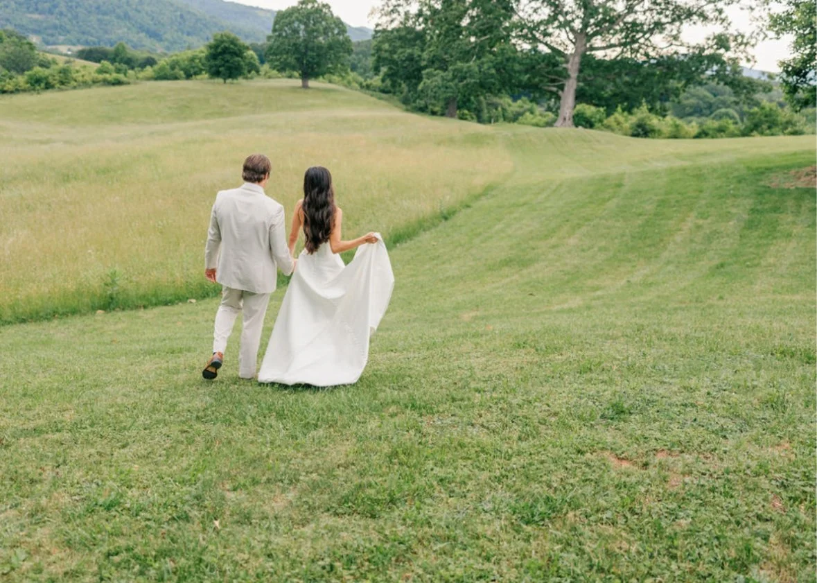 A bride and groom walking together on a grassy hill in a scenic outdoor setting.
