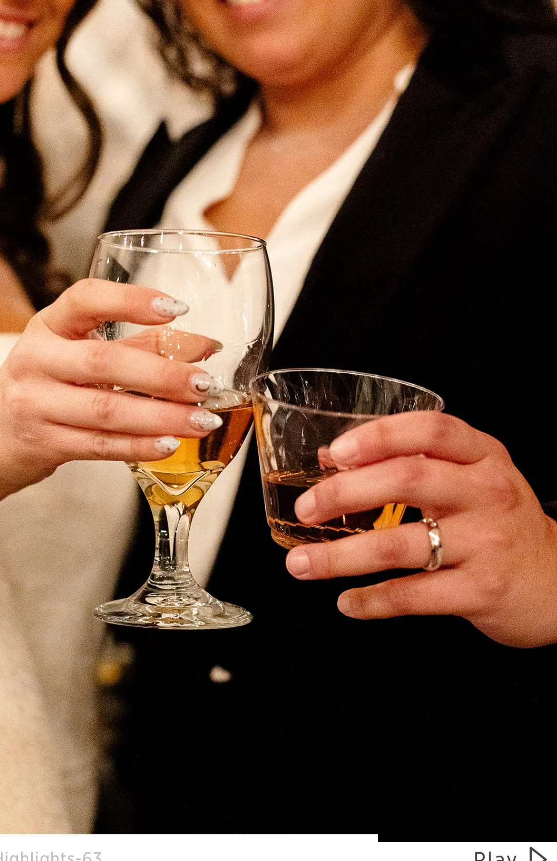 Two women holding glasses of wine, one with a glass of white wine and the other with a glass of amber-colored wine, dressed in formal attire at a social gathering.