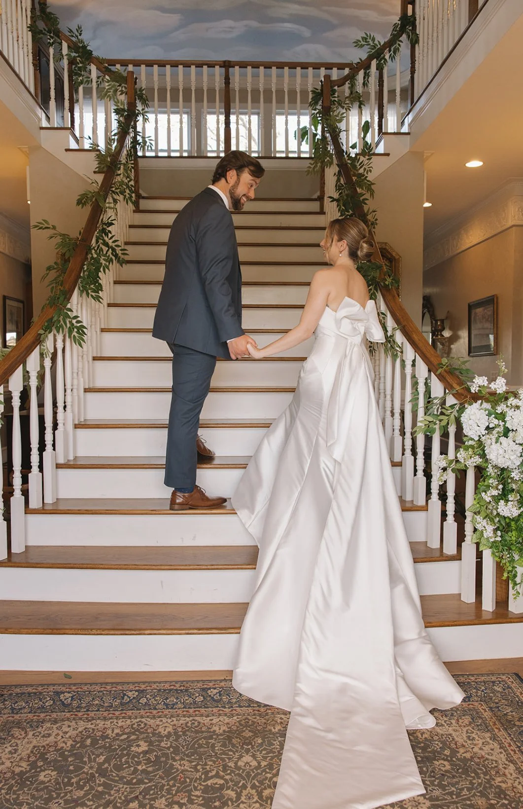 A bride and groom holding hands on a staircase inside a decorated wedding venue.