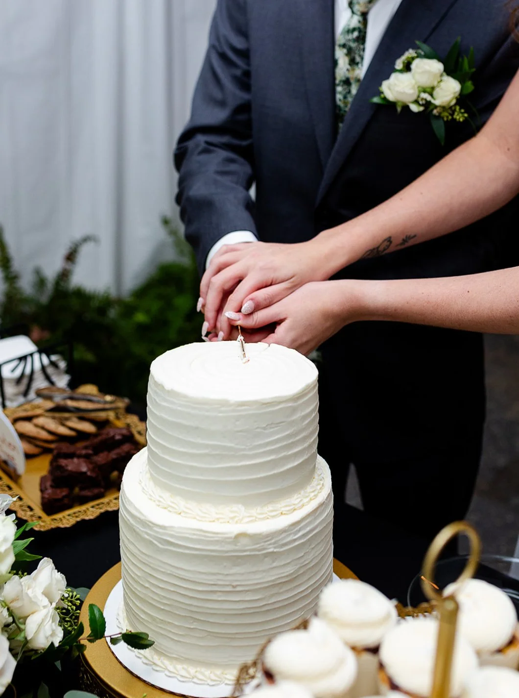 A bride and groom cutting a wedding cake together, with the bride's hand on top of the groom's hand.