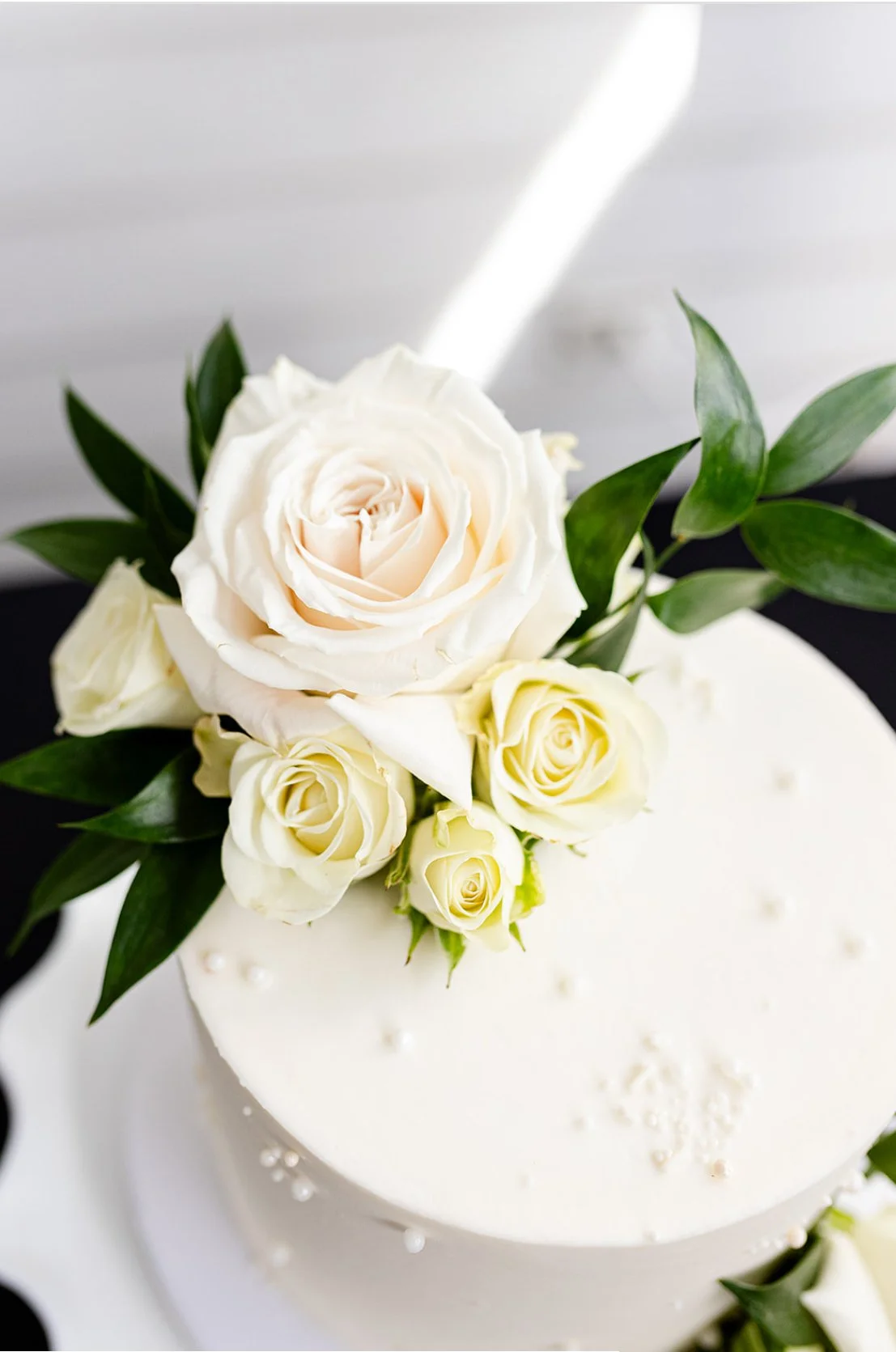 A white wedding cake decorated with white roses and green leaves.