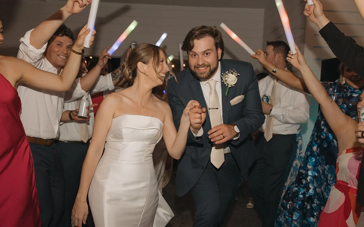 A bride and groom are dancing together surrounded by guests at a wedding reception, with guests holding light-up sticks.
