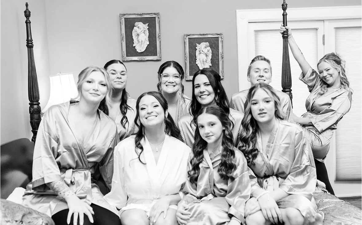 A group of women and girls wearing matching satin robes in a bedroom, smiling for a photo.