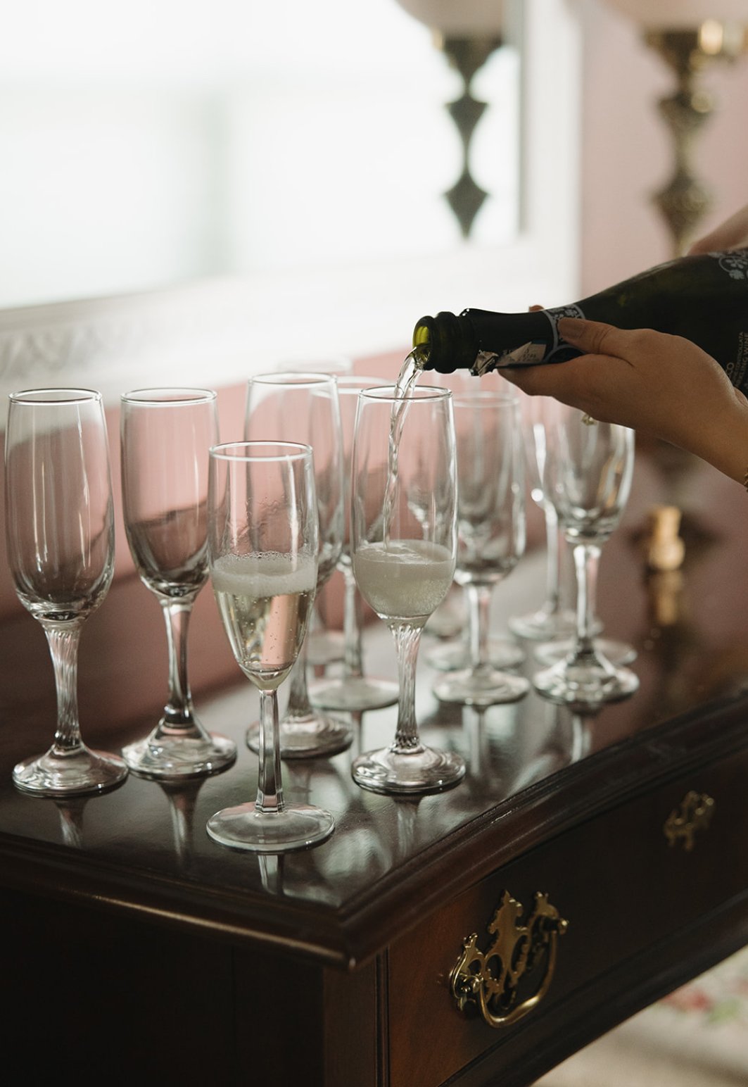 Person pouring champagne into glasses on a dark wooden table.