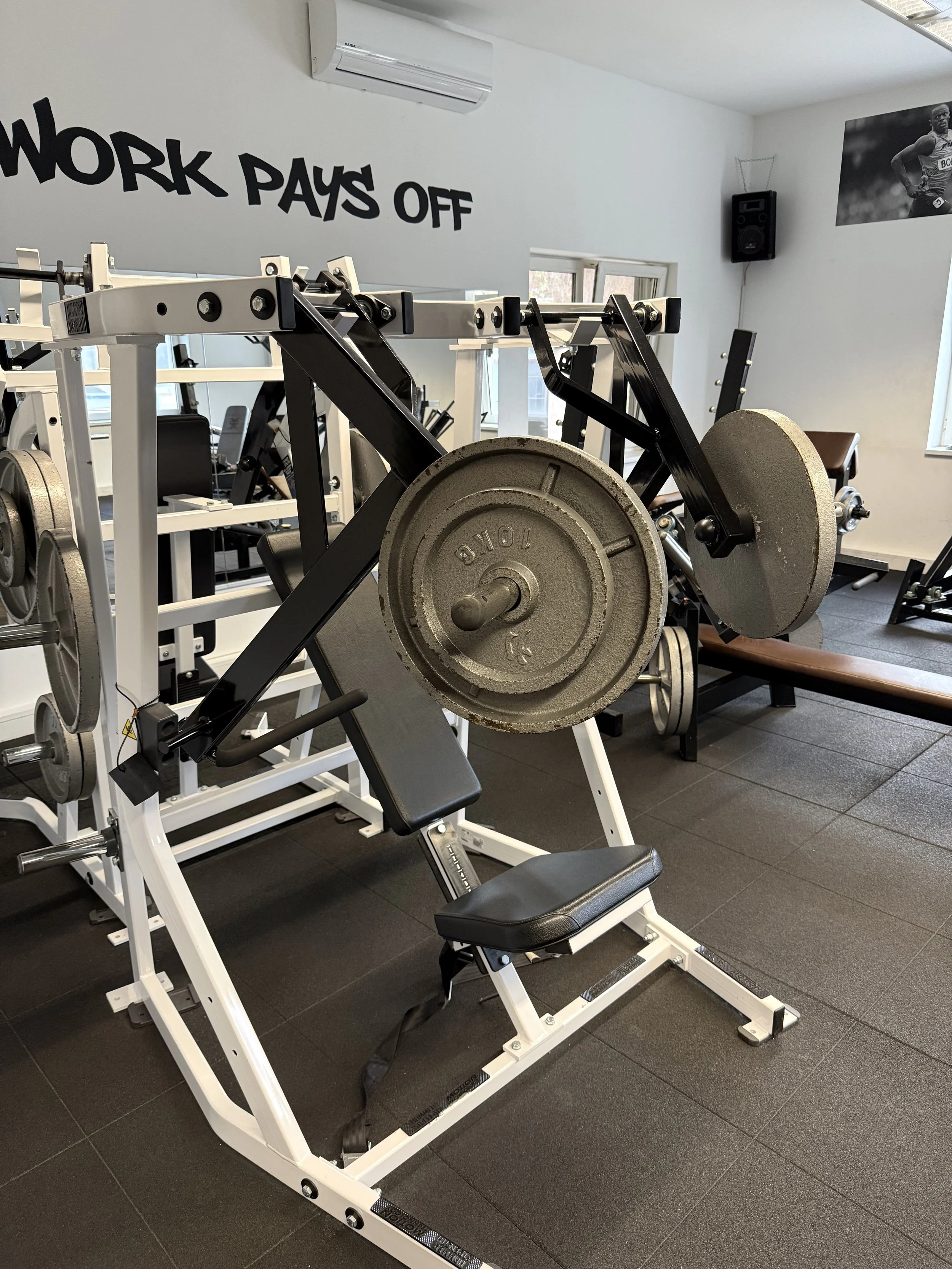 Gewichtheberbank mit Gewichtsscheiben im Fitnessstudio, Wand mit Spruch 'HARD WORK PAYS OFF' und Sportposter