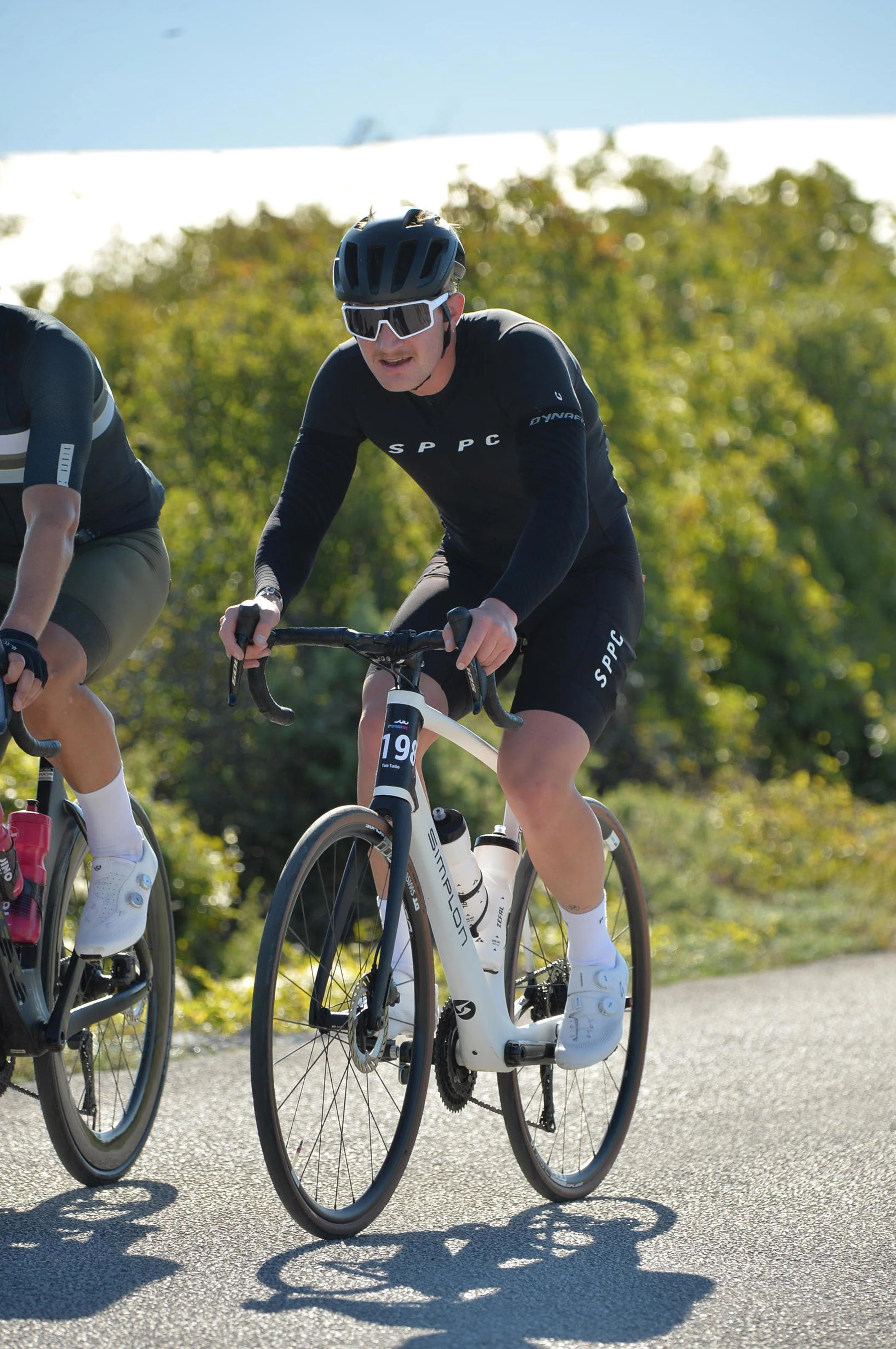 Mann beim Radfahren auf einer Straße, trägt einen Helm, Sonnenbrille und ein schwarzes Fahrradtrikot.
