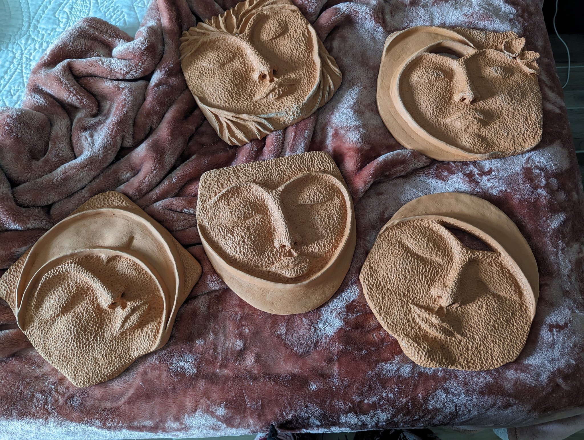 Five round clay sculptures with carved faces resting on a flour-dusted brown blanket.