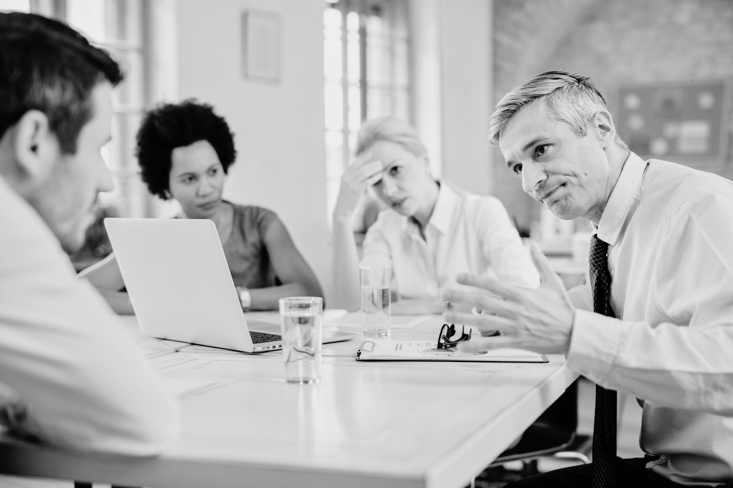 Four people engaged in a serious discussion during a meeting in an office, with two women and two men, one of whom is speaking.