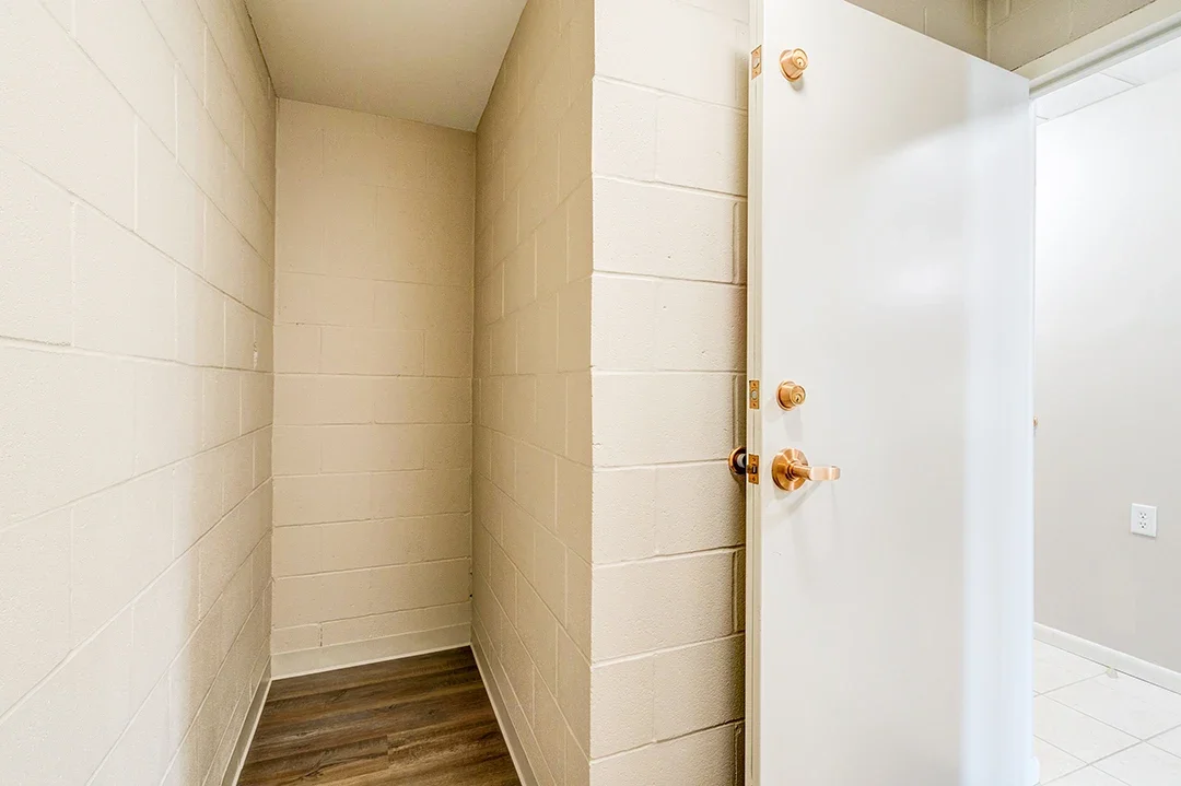 An empty nook with cinder block walls and a wooden floor, partially enclosed by a door that is slightly open.