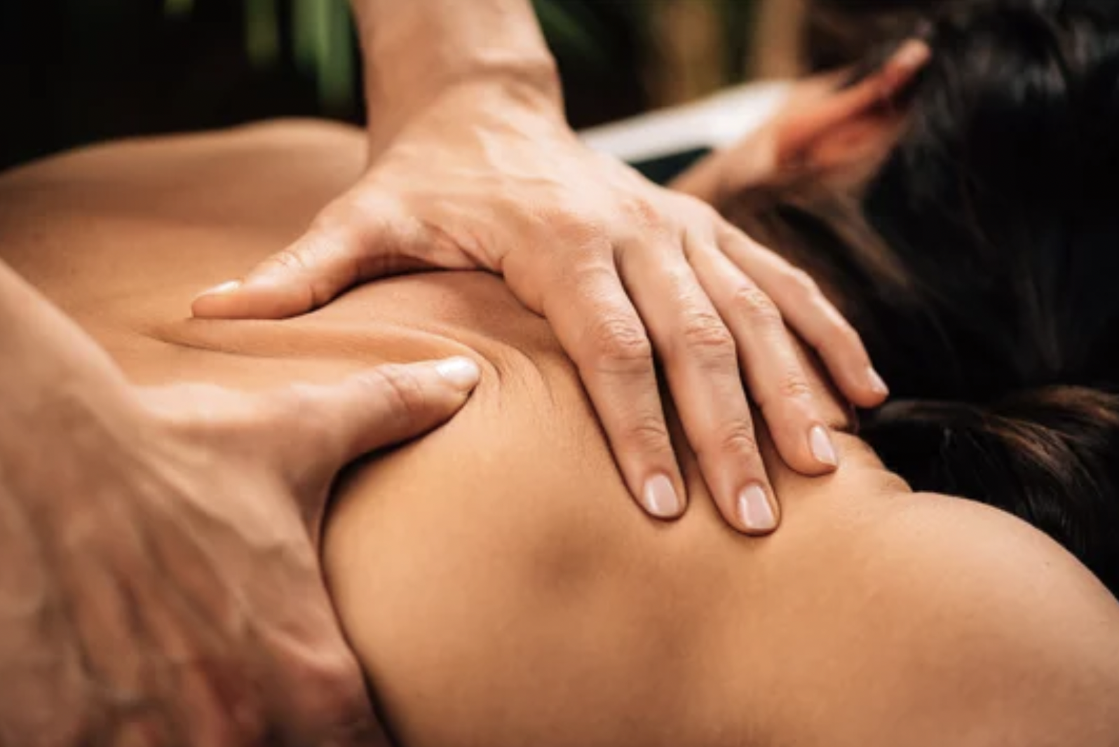 Close-up of a person receiving a massage on their shoulder from a massage therapist.