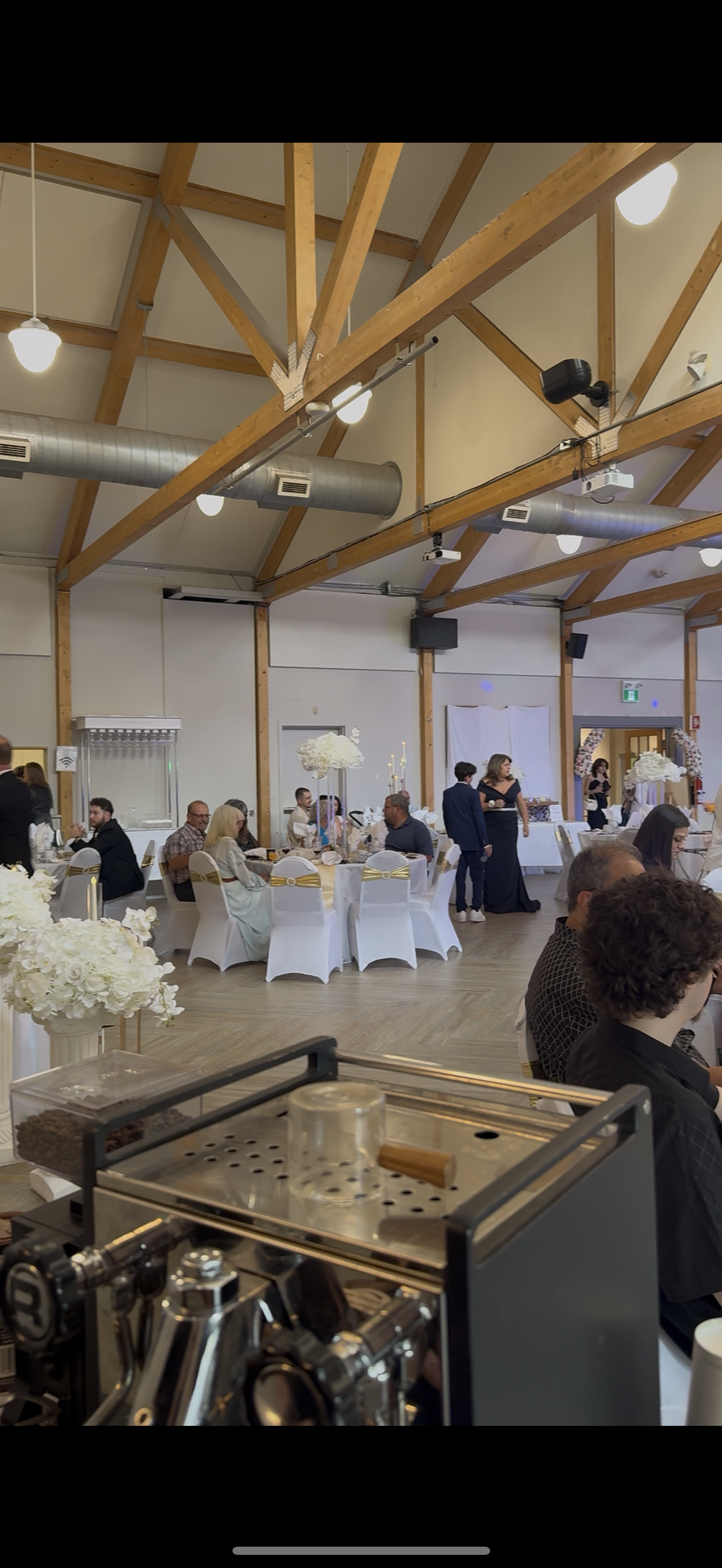 Premium espresso and matcha catering at a formal wedding reception in Hudson, QC. Guests seated at elegant tables with floral centerpieces in a rustic event hall with wooden beams, featuring professional specialty coffee services by Cafe Apero.