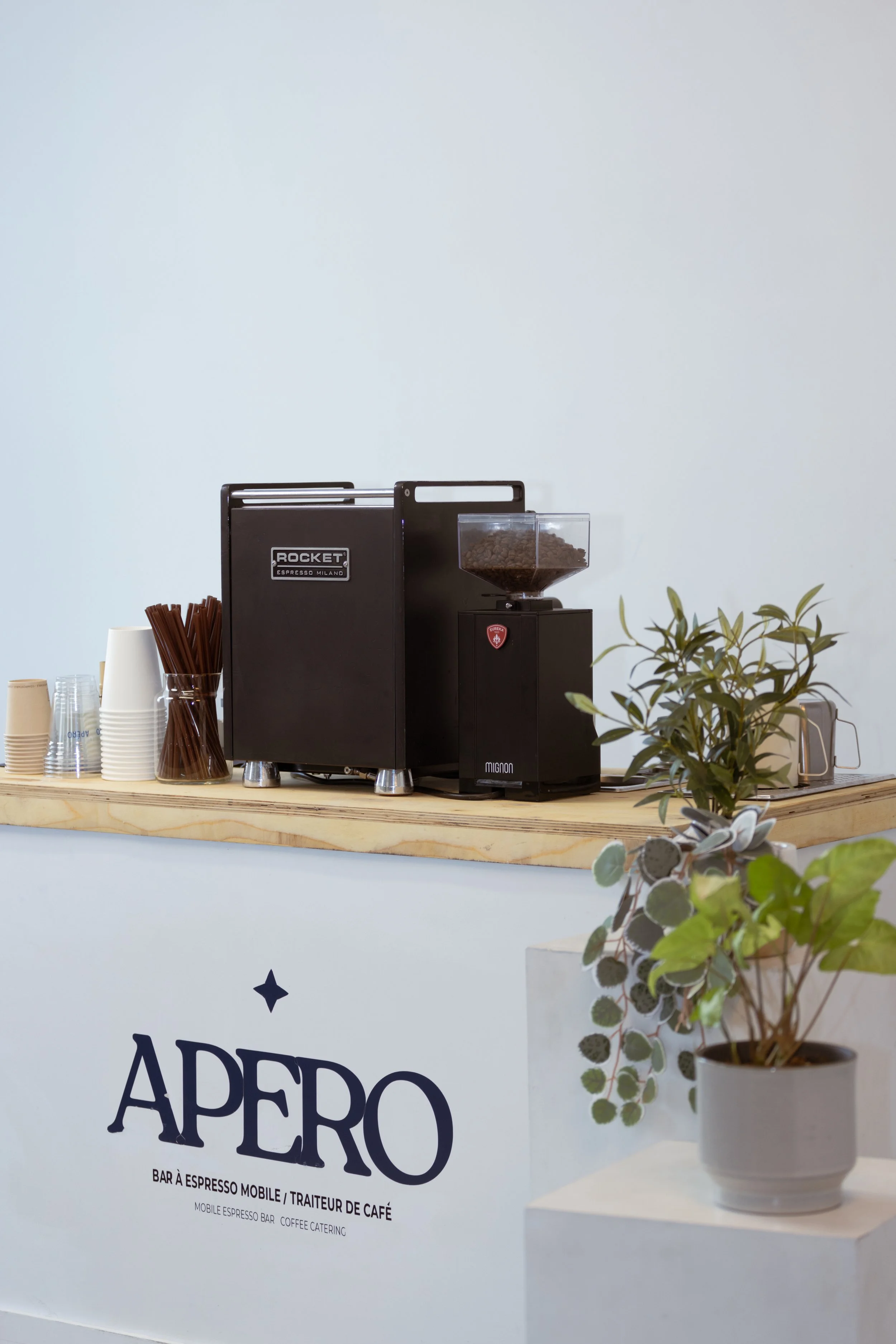 Coffee machine, cups, and plants on a wooden counter at a coffee shop named APERO.