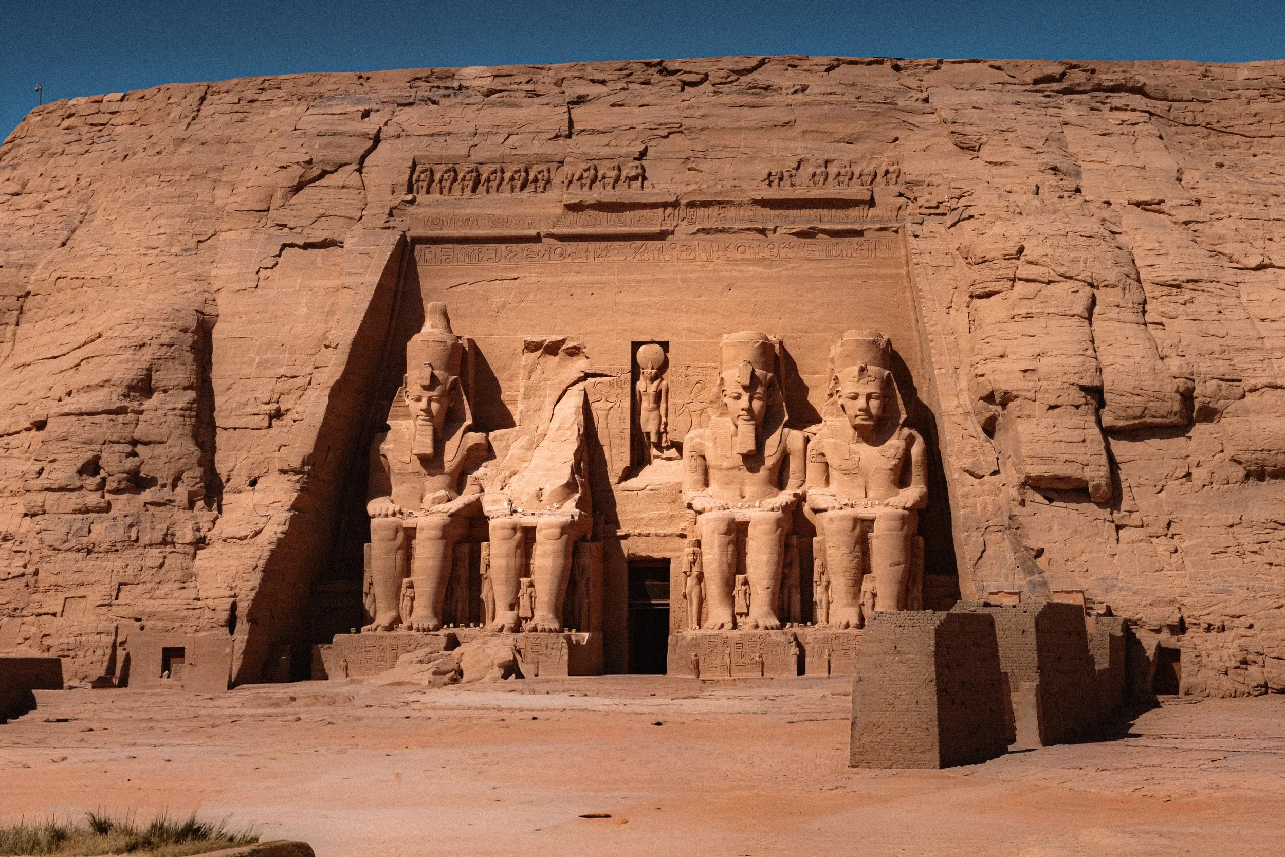Ancient Egyptian temple with large statues of pharaohs carved into the stone facade, set against a blue sky.