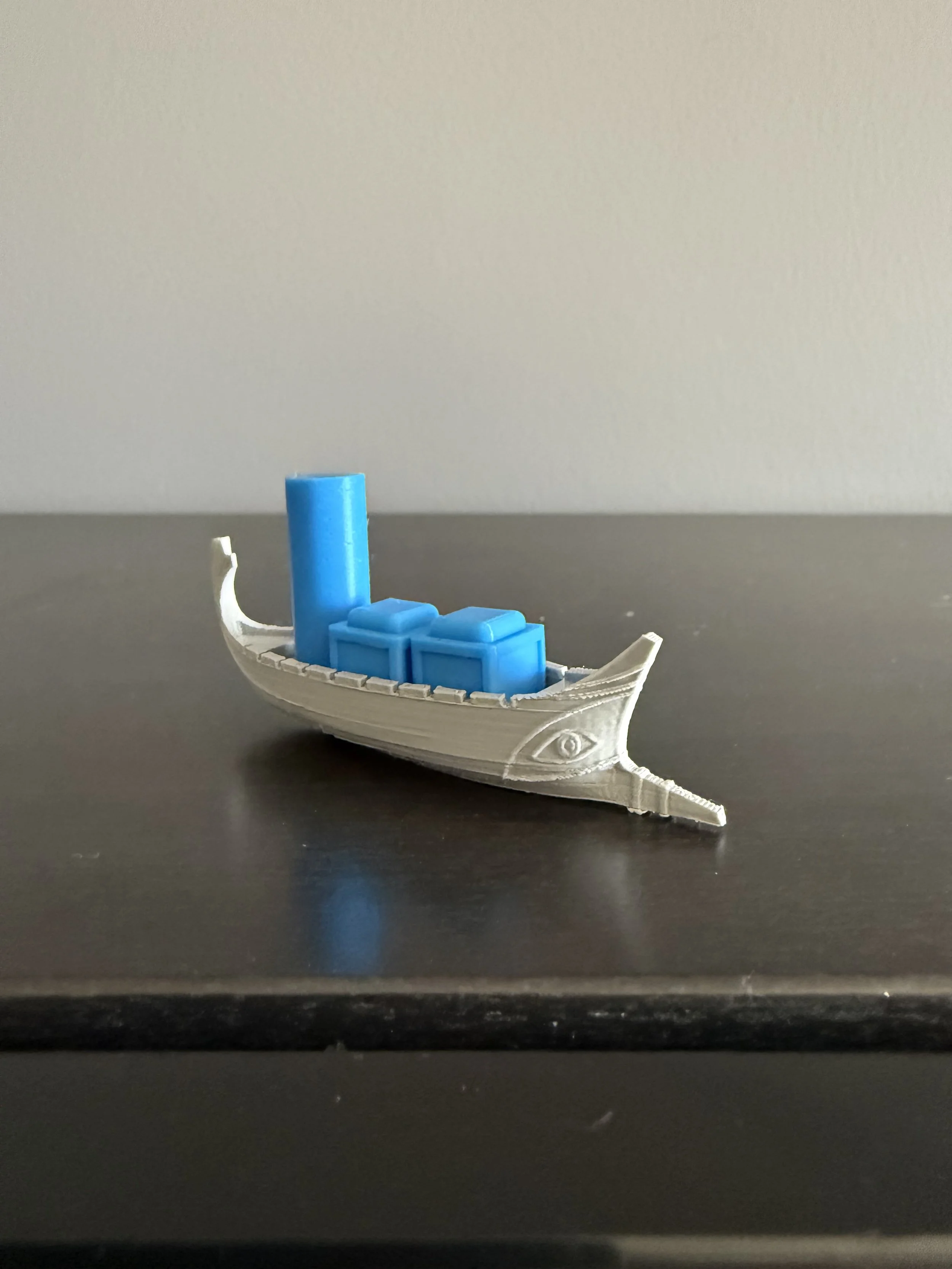 Small toy gondola boat with blue containers on dark surface against light background.