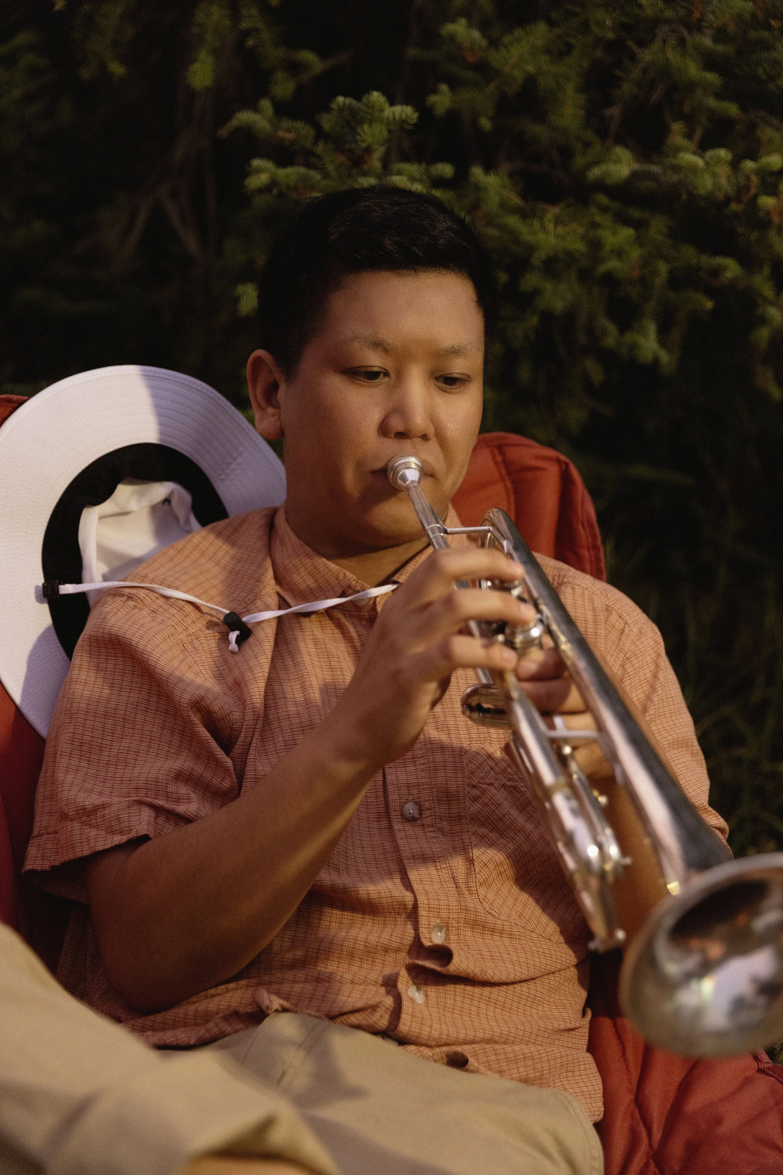 A young person outdoors playing a silver trumpet.