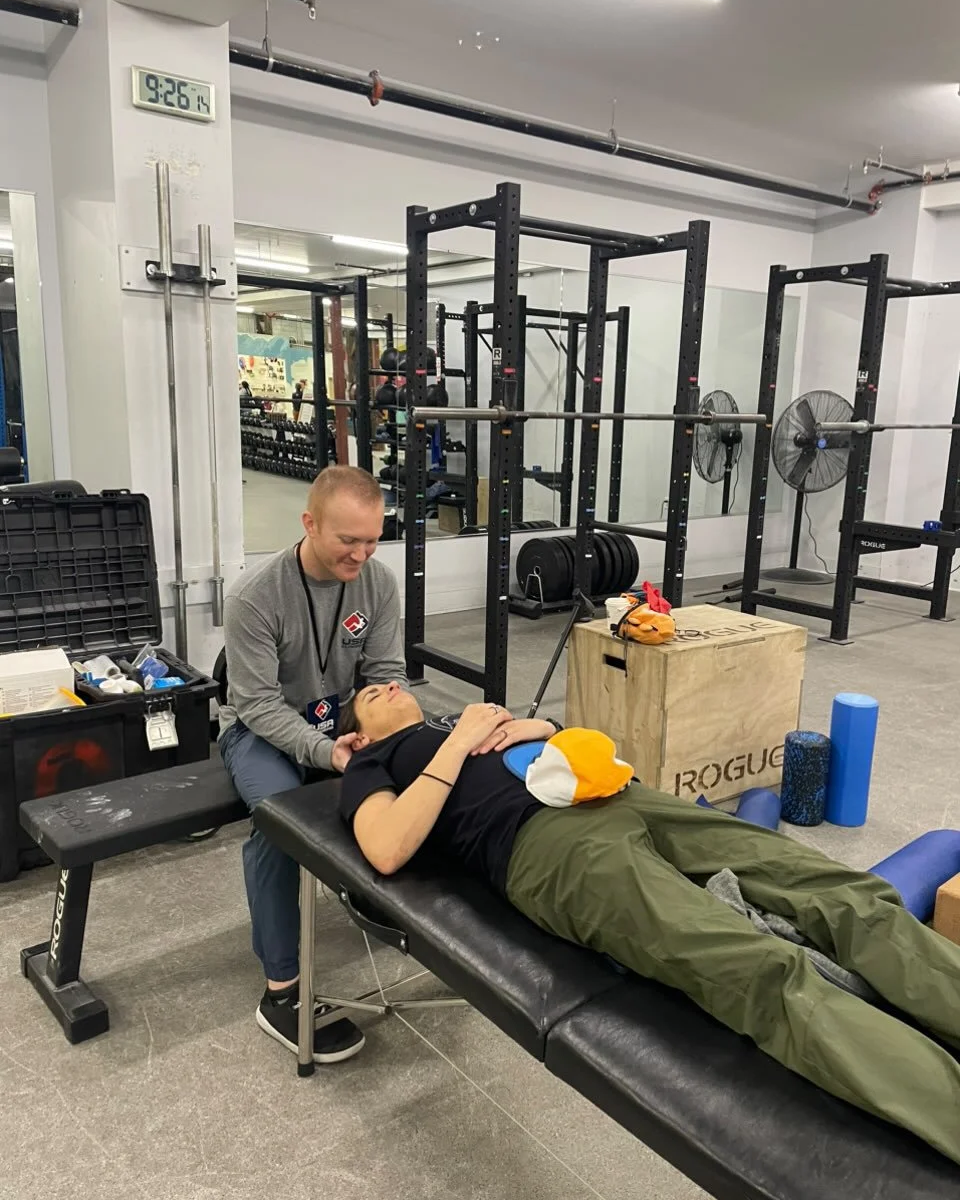 A person lying on a treatment table in a gym, receiving a physical therapy or chiropractic adjustment from a practitioner.