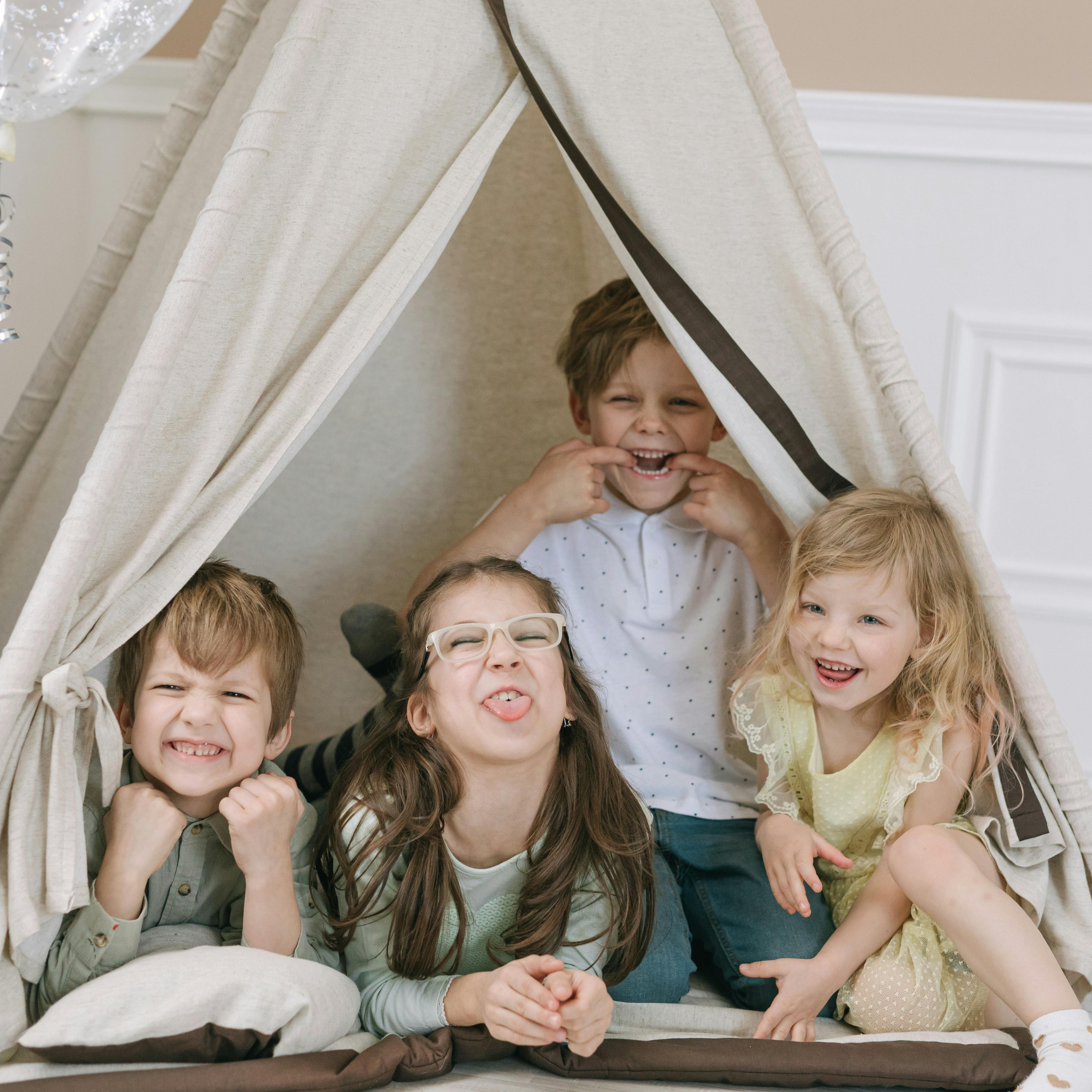 Four children sit inside a fabric play tent, smiling and making funny faces at the camera for pediatric airway and tongue-tie care.