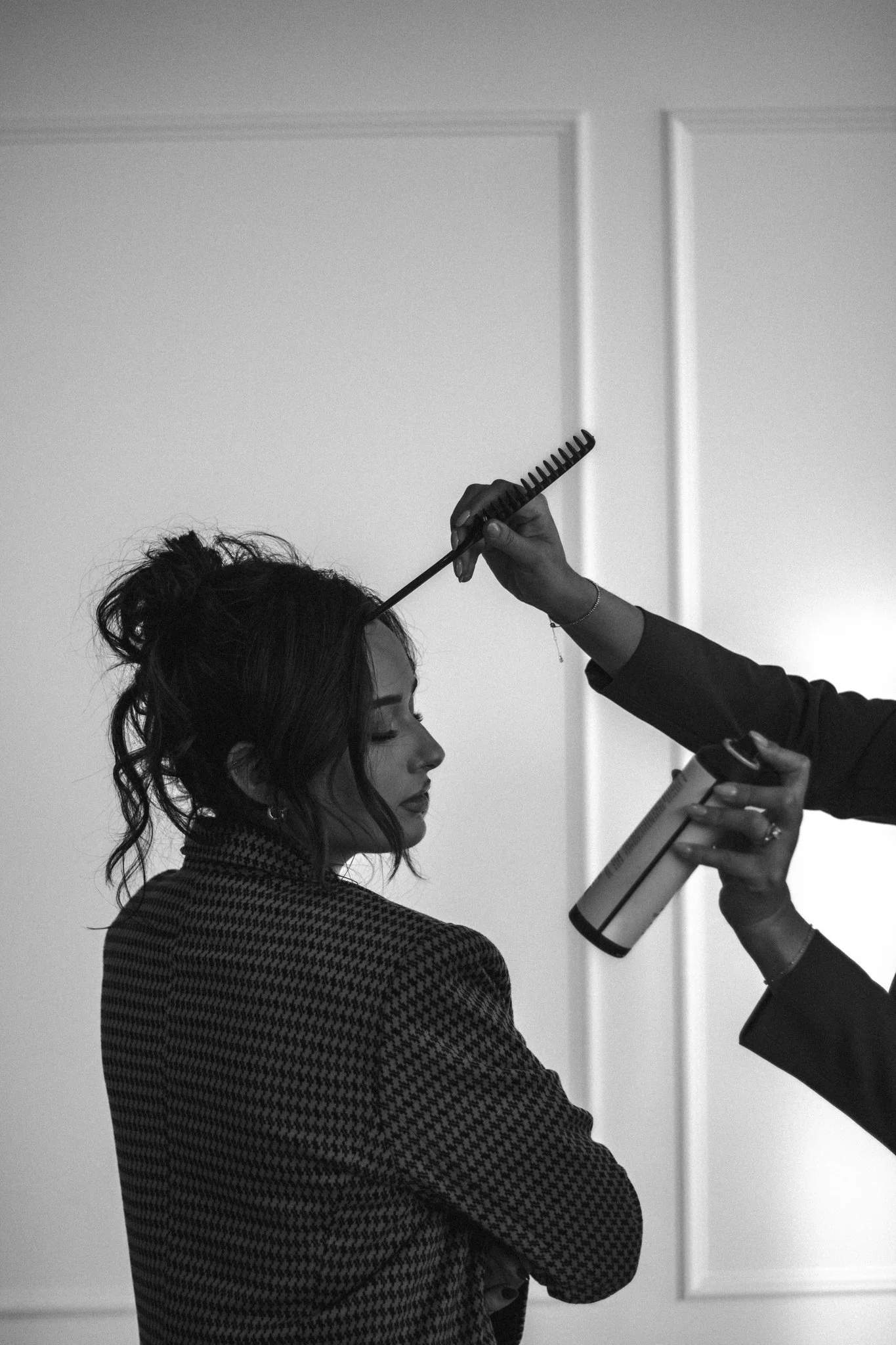 A woman getting her hair styled with a hair spray and a comb in a salon.