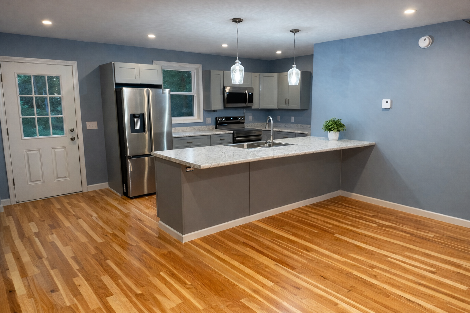 Modern kitchen with blue walls, hardwood floors, stainless steel refrigerator, microwave, and oven, gray cabinets, marble countertop island, and a small potted plant.