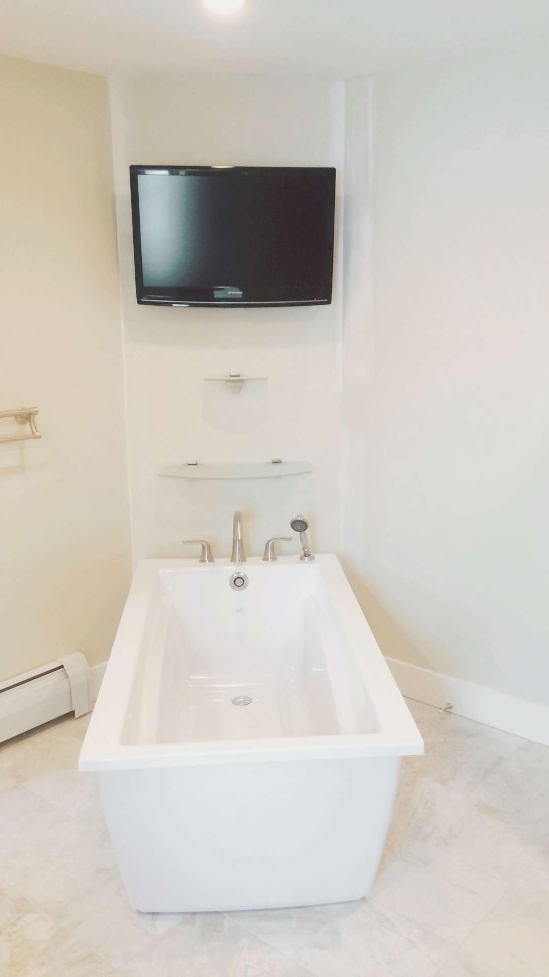 Bathroom with a white bathtub, wall-mounted flat-screen TV, and a small shelf above the tub.