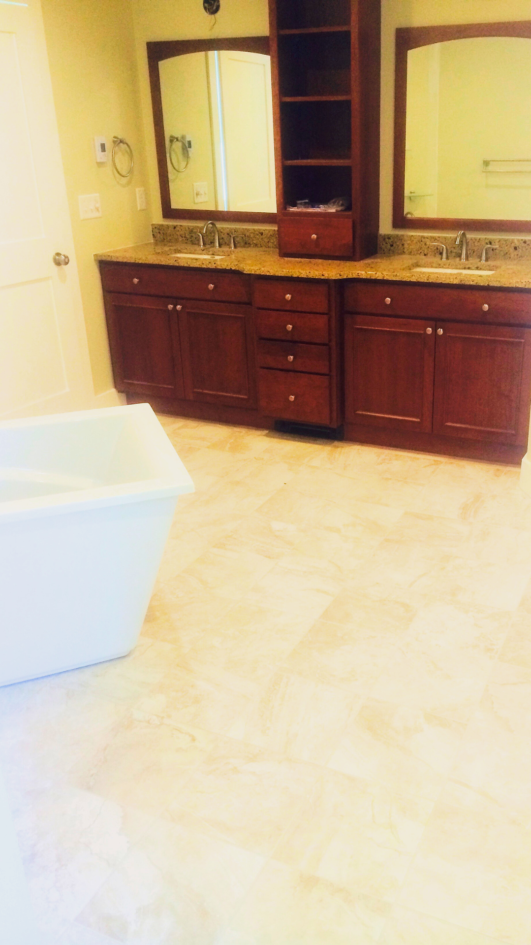 Bathroom with a double vanity, granite countertop, large mirror, wooden cabinets, and a white bathtub.